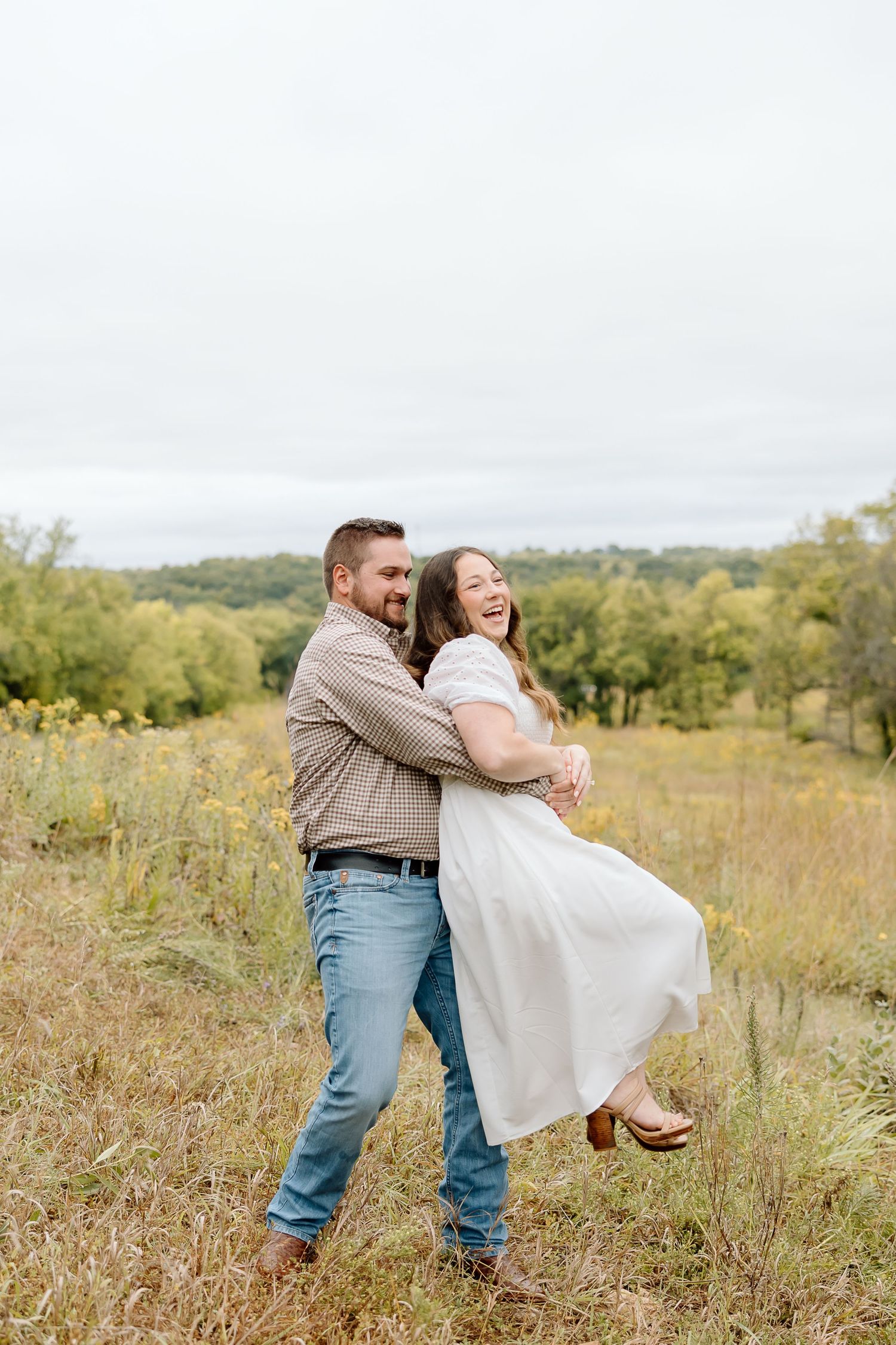 Couple shares playful moment with lift pose in wildflower field.