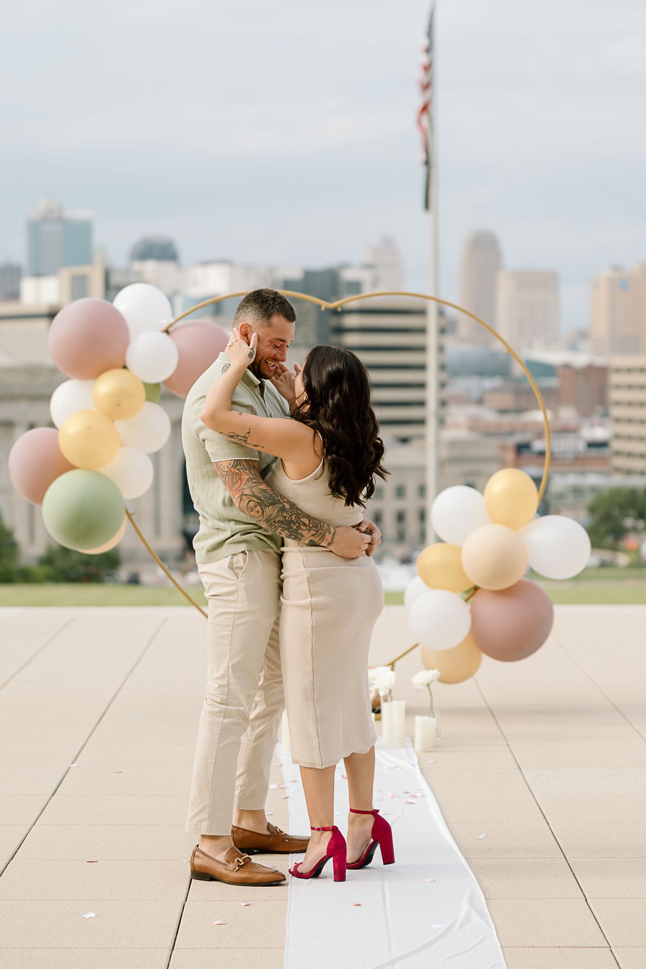 Couple sharing intimate moment on urban rooftop surrounded by soft colored balloons.