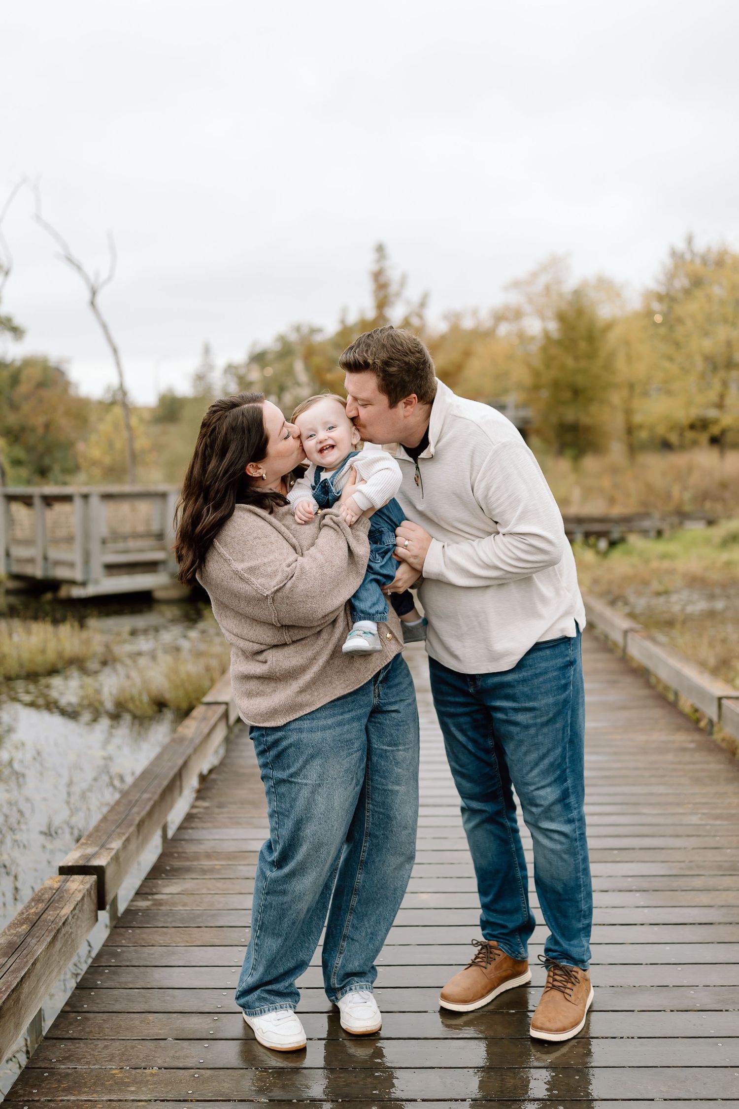 A family shares tender moments together on a wooden boardwalk surrounded by autumn foliage.