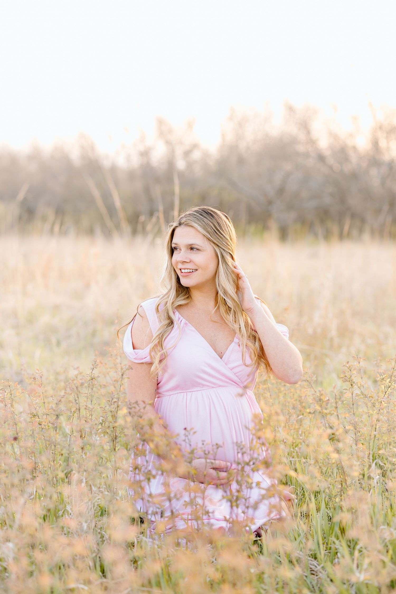 A person in a pink dress sits gracefully among wildflowers in a sunlit meadow during golden hour.
