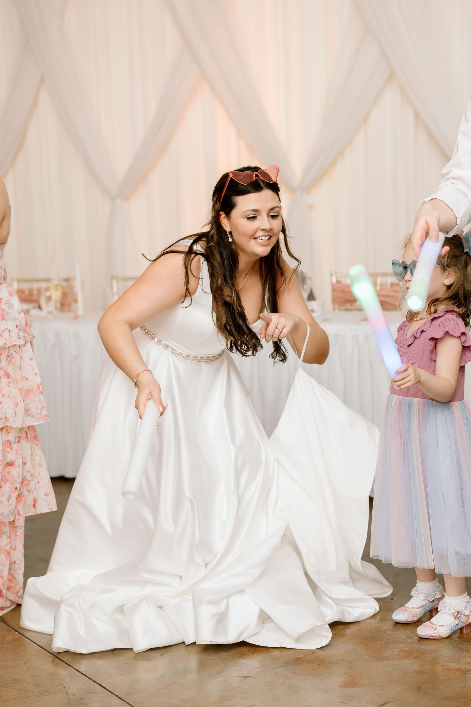 A person in a flowing white wedding dress dances joyfully on a wooden dance floor at a reception.
