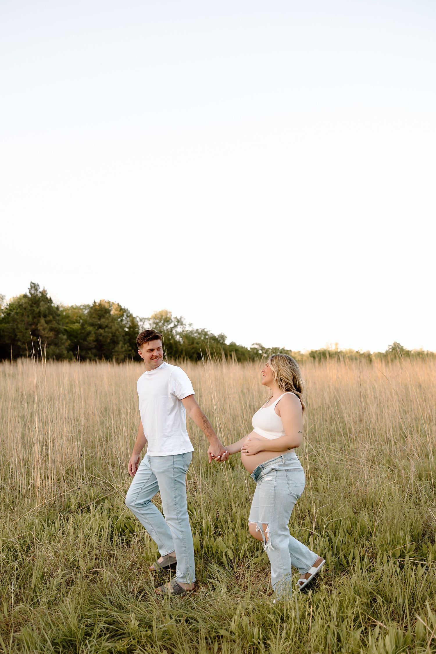 A couple shares playful moments in a golden field of tall grass during sunset.