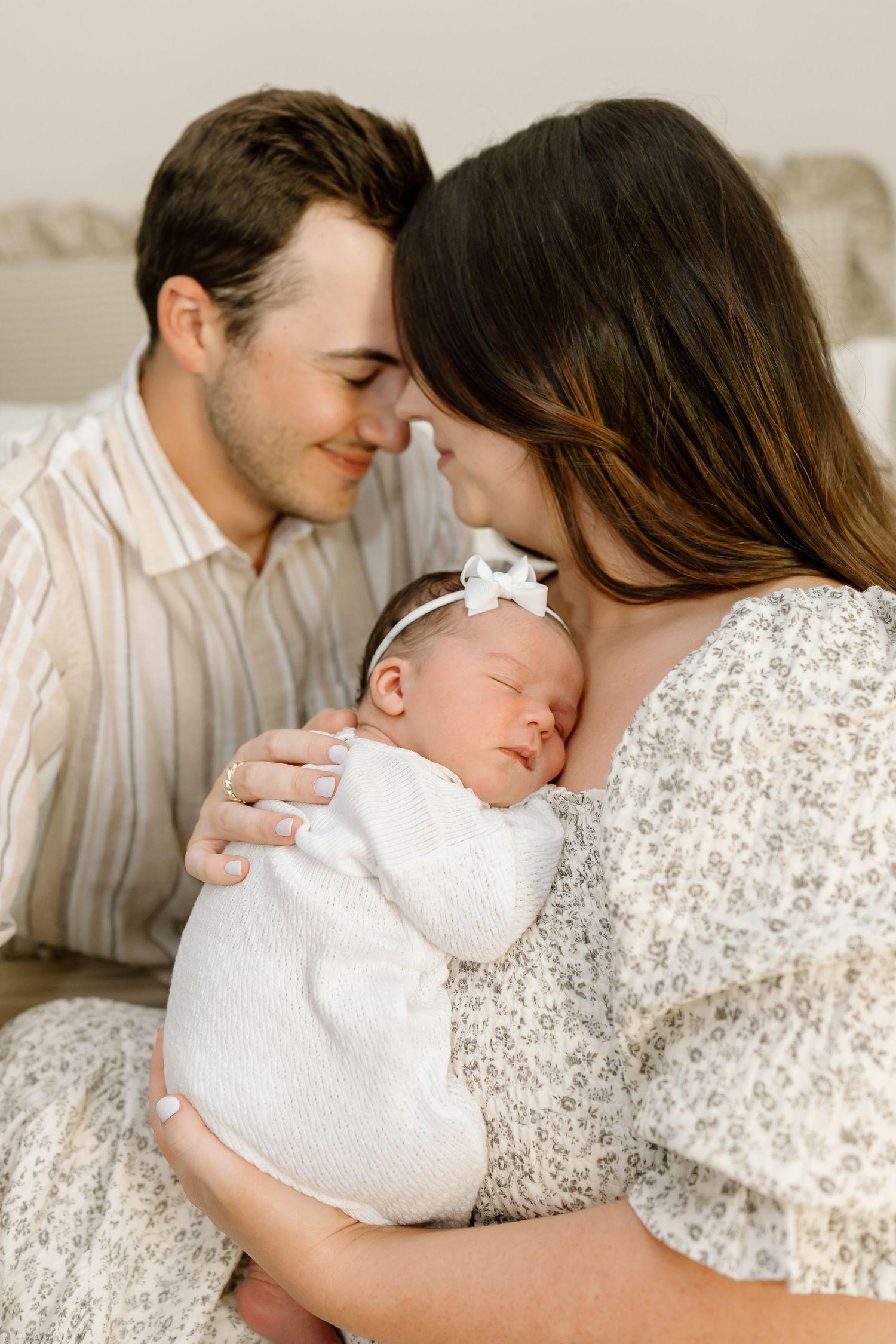 A series of tender moments between a parent and sleeping baby in white against a neutral background.
