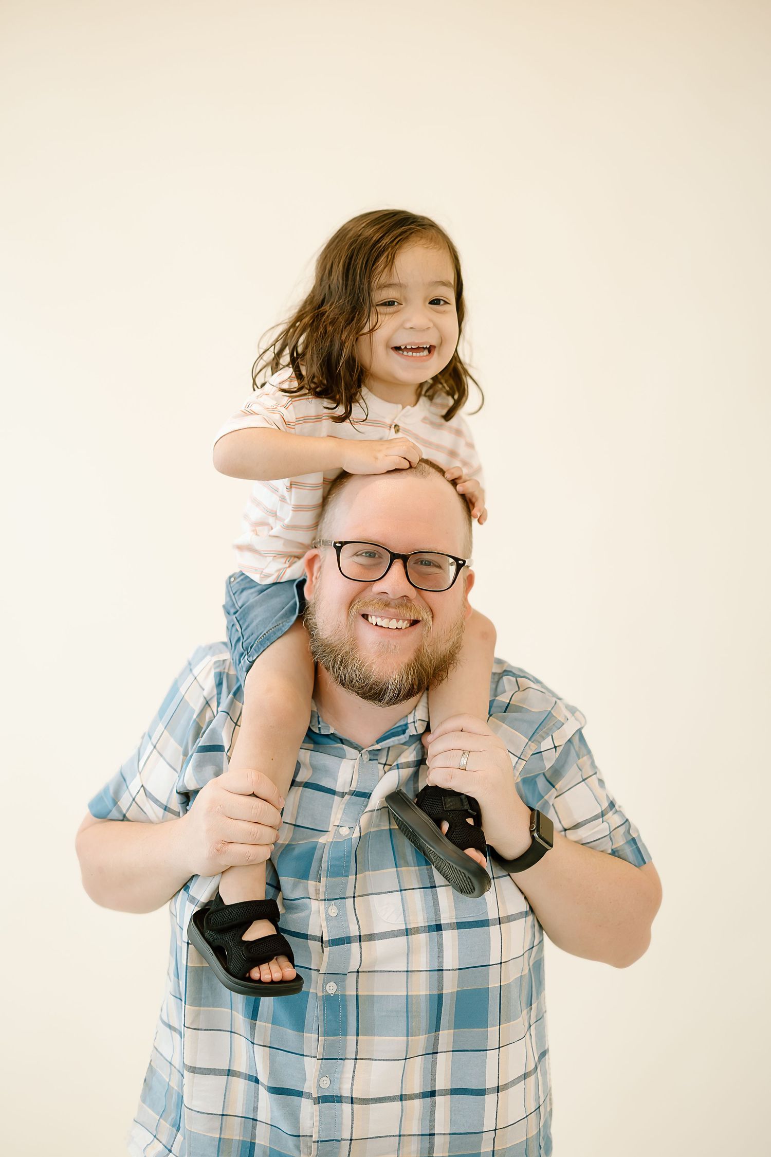 A heartwarming moment captured as a child sits on shoulders against a light background.