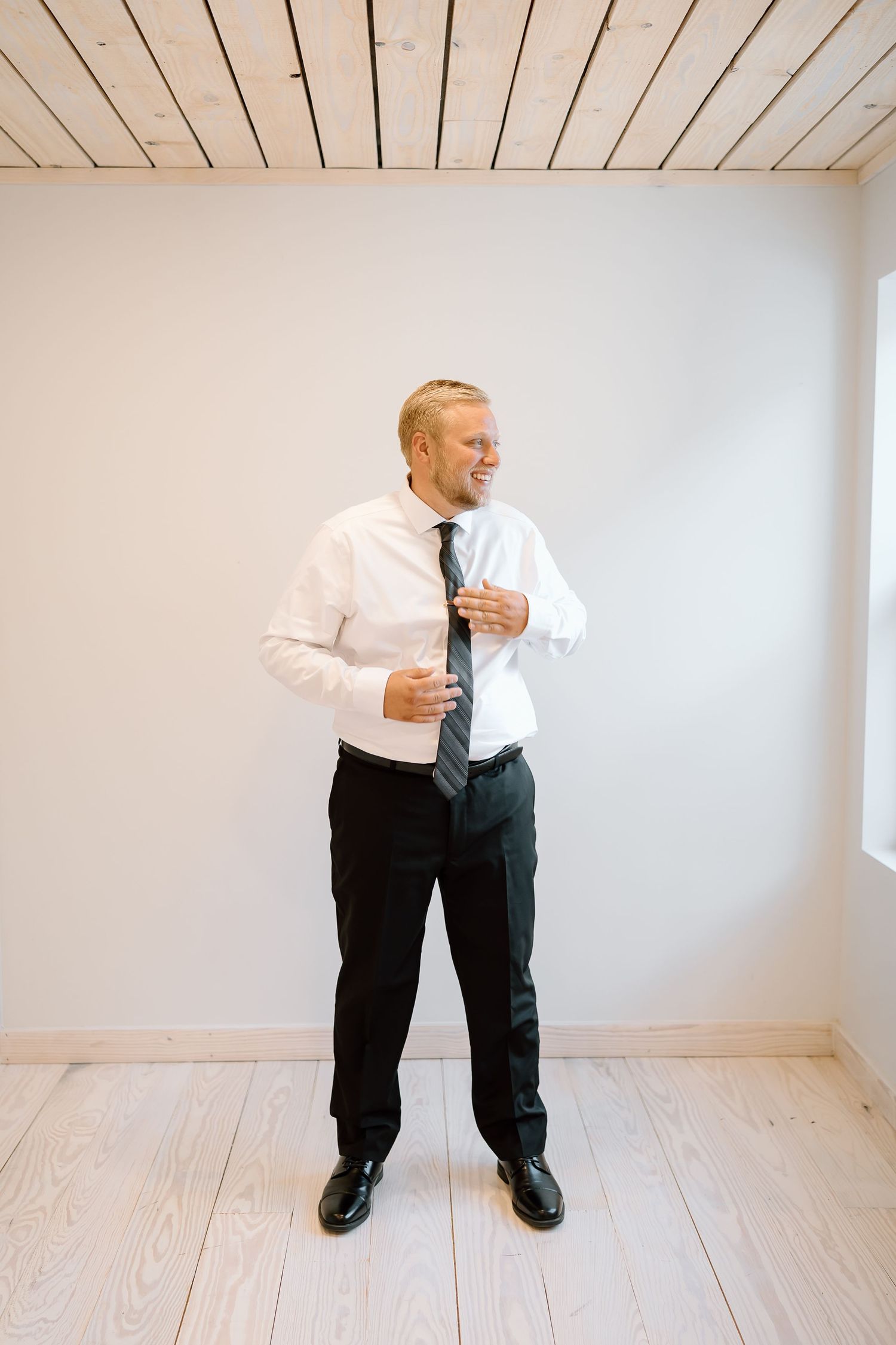 A person in business attire stands in an empty white room with wooden floors in a sequence of four connected photos.