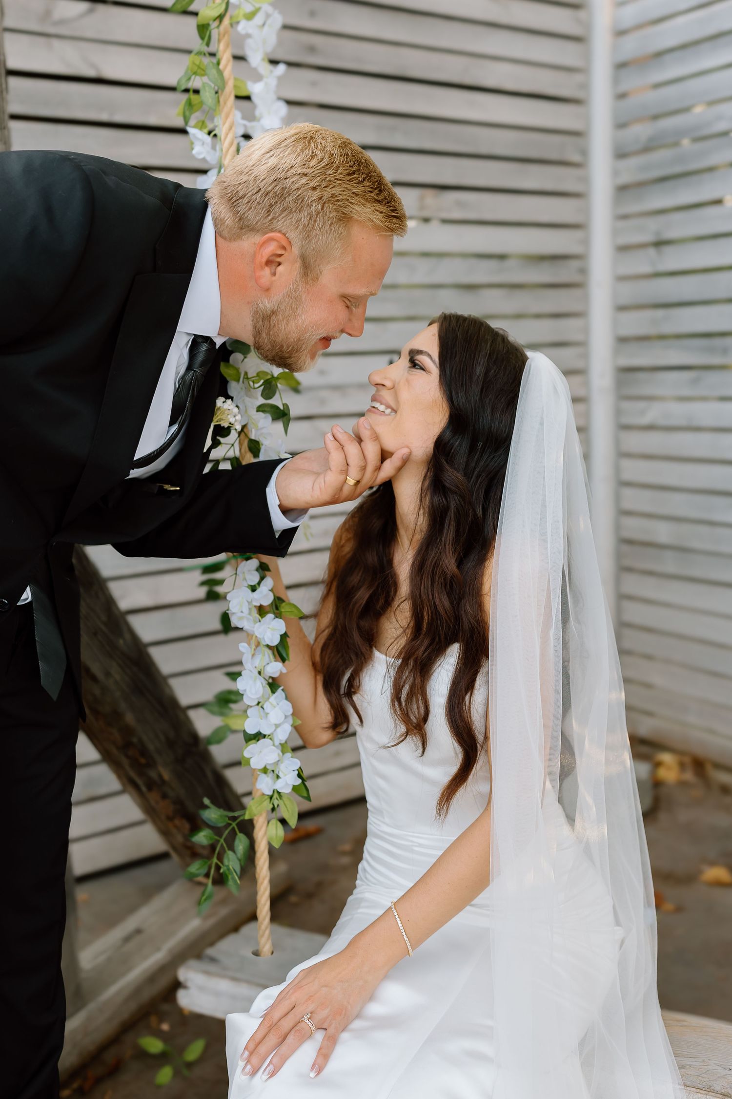 A romantic wedding couple shares tender kisses in a series of photos against a white siding wall.