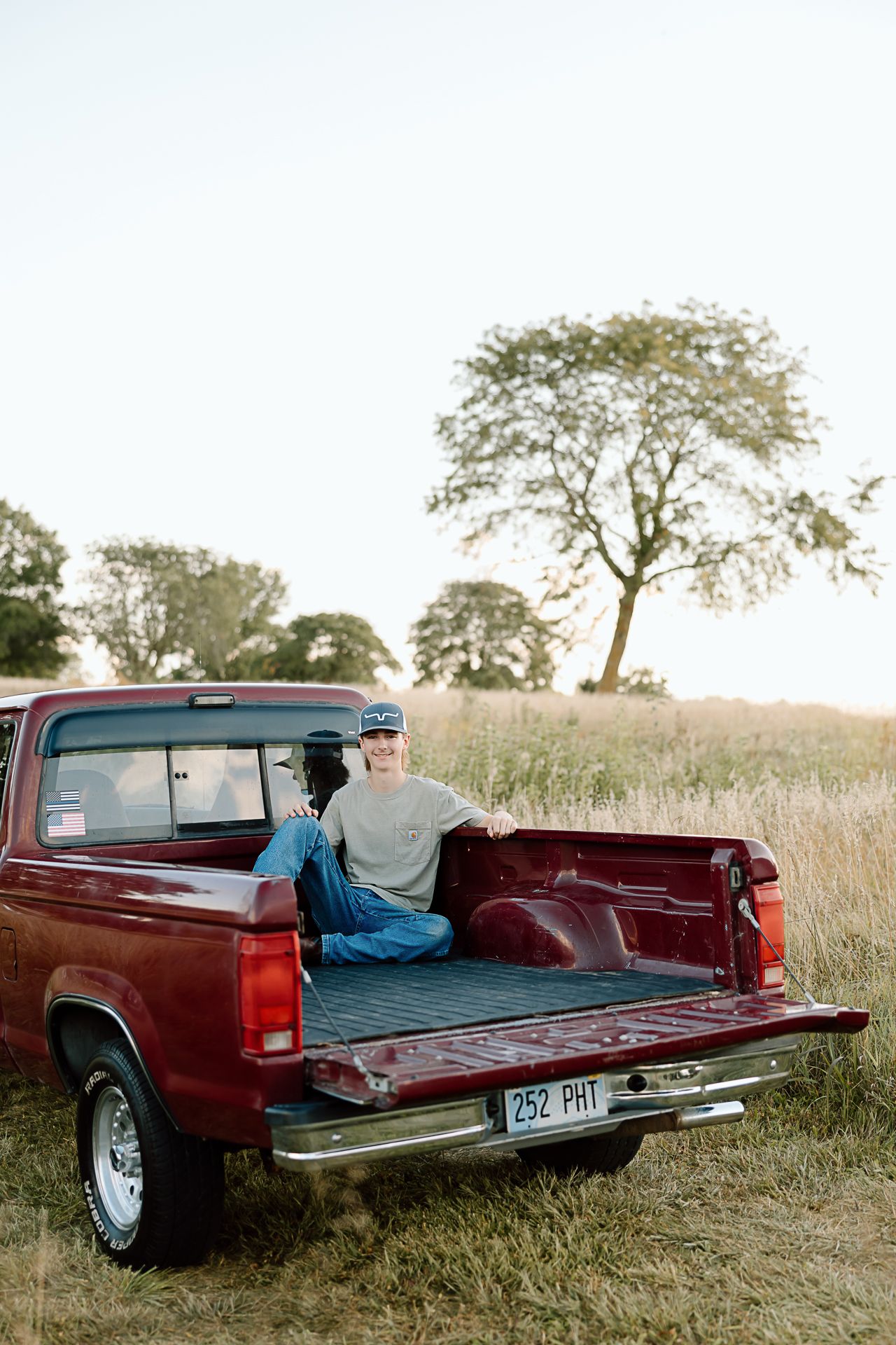 Someone sitting in the bed of a classic red pickup truck during sunset in a rural field.
