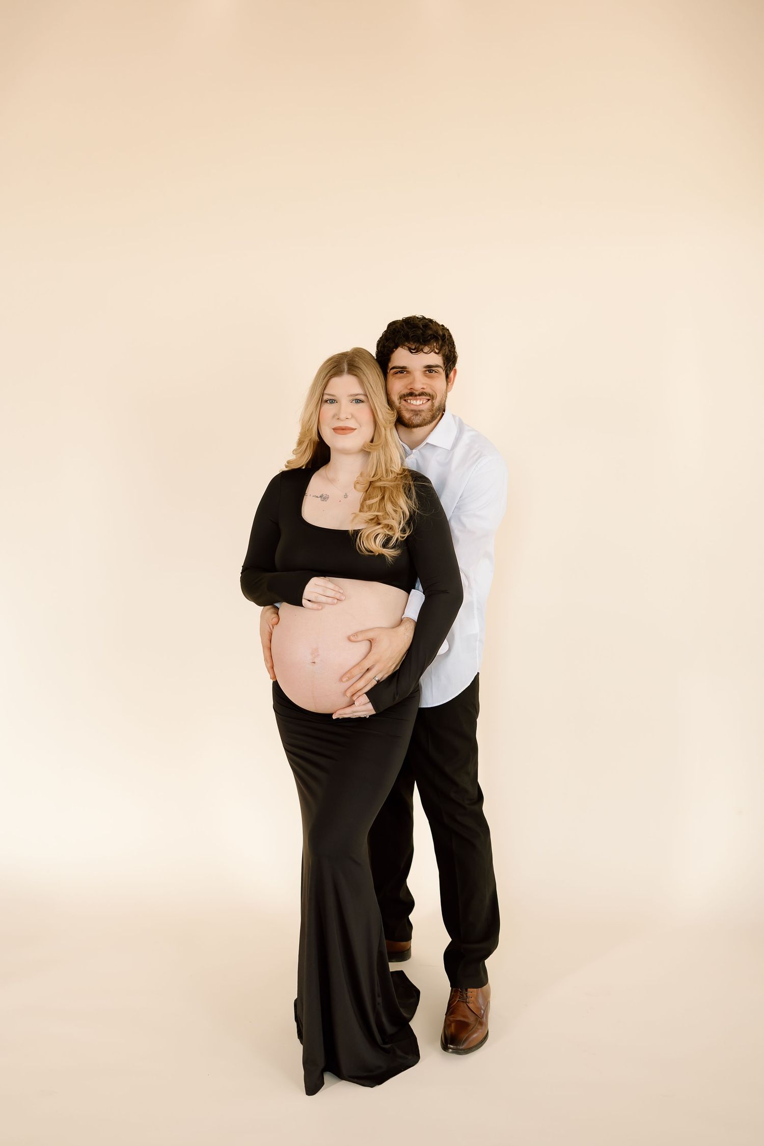 Maternity portrait of couple in black and white outfits against neutral background.