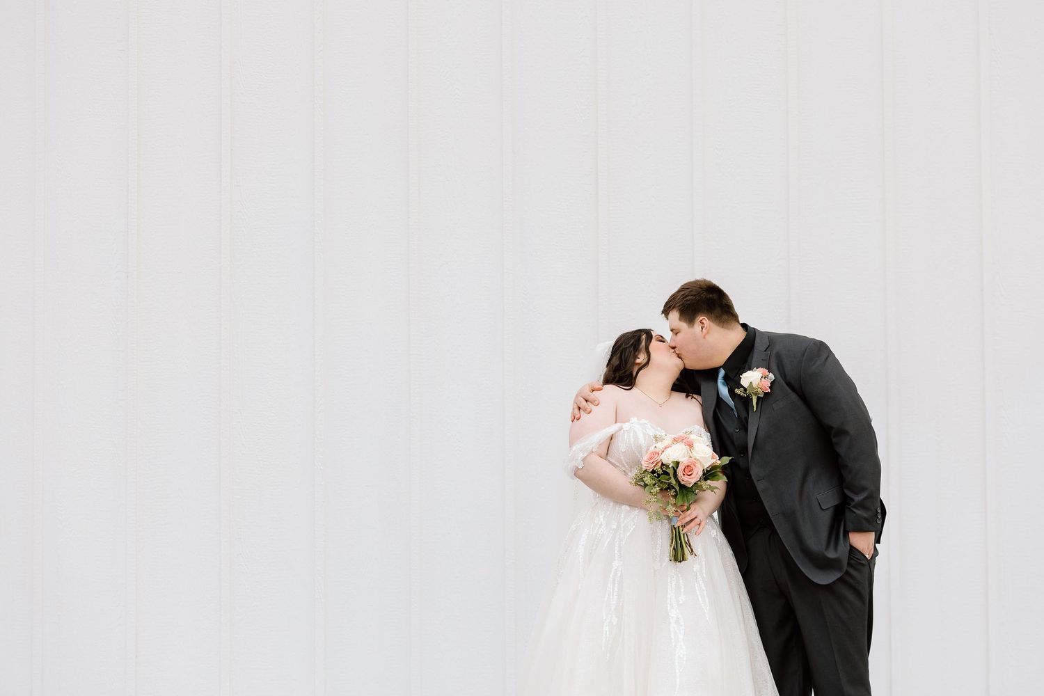 Intimate moment between newlyweds against minimalist white wall background.