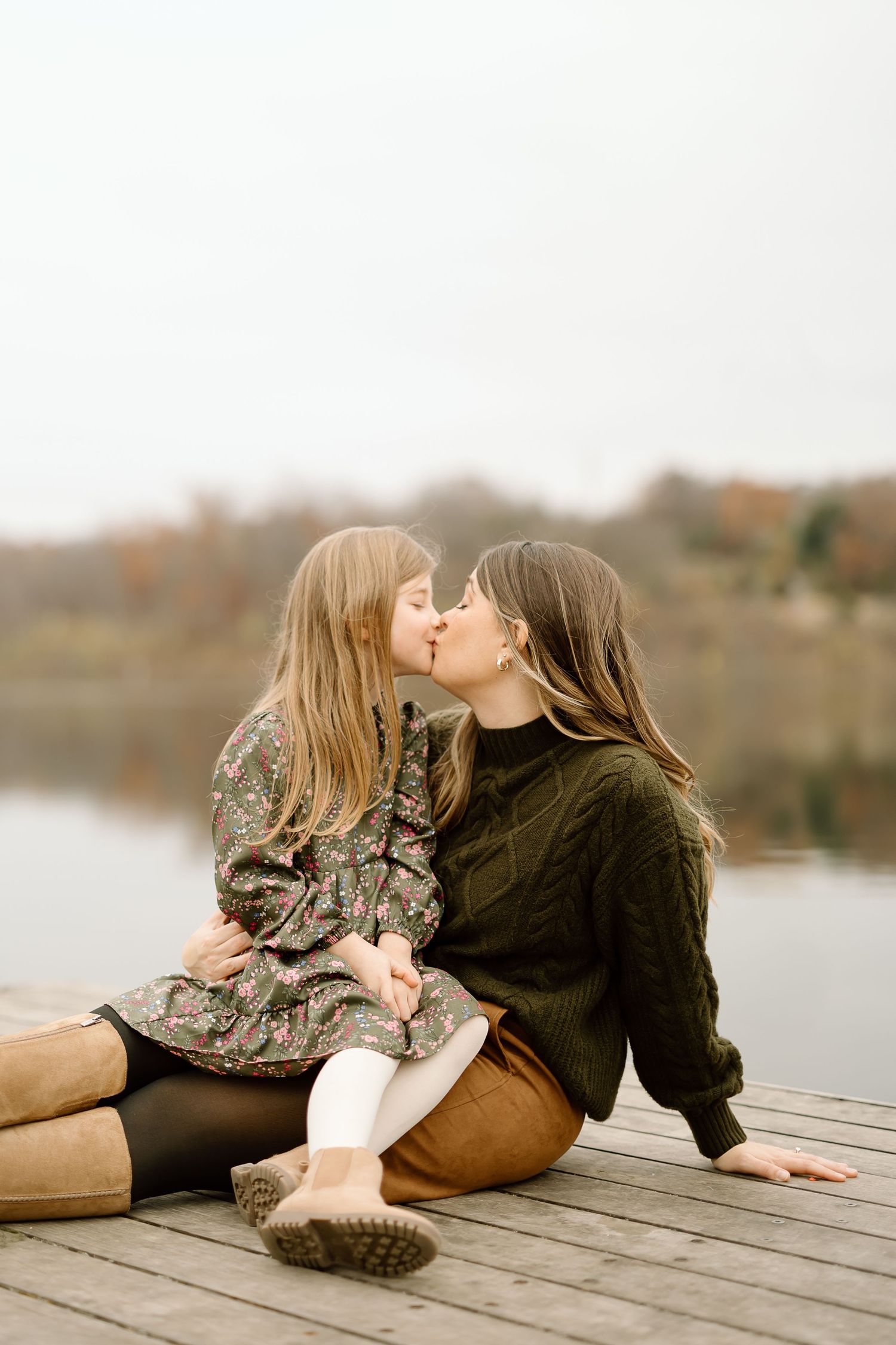 Tender moment shared between parent and child sitting on wooden dock by calm waters.
