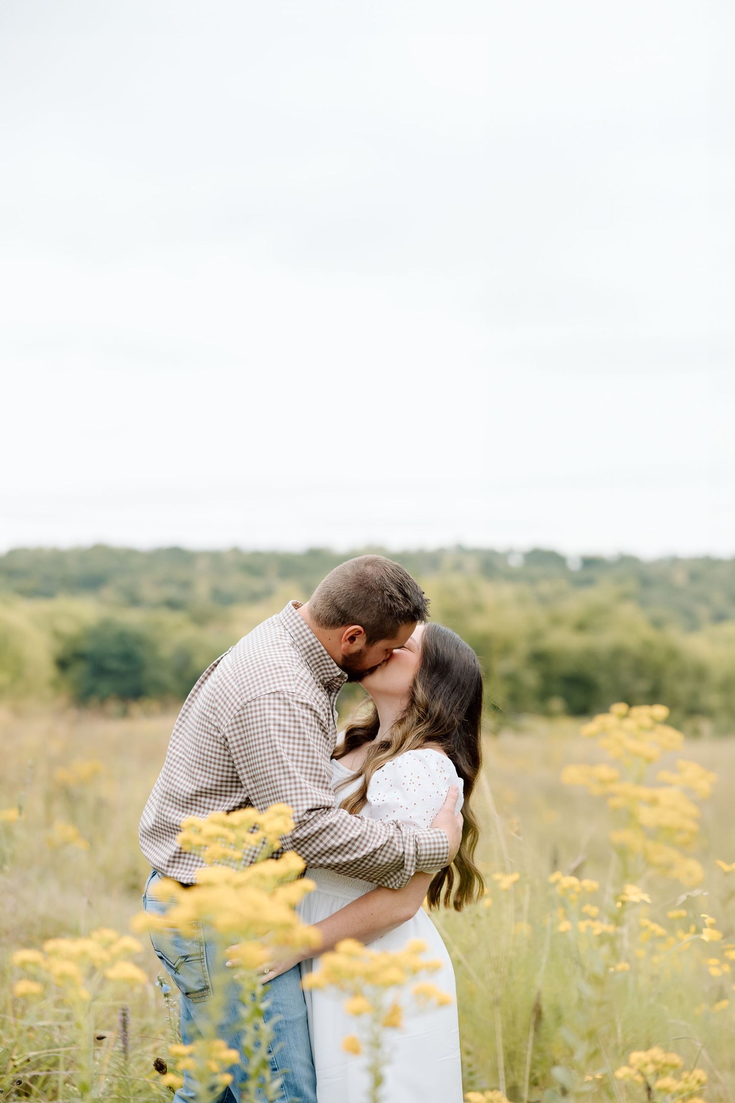 Romantic embrace captured in golden meadow with soft natural lighting and yellow flowers.