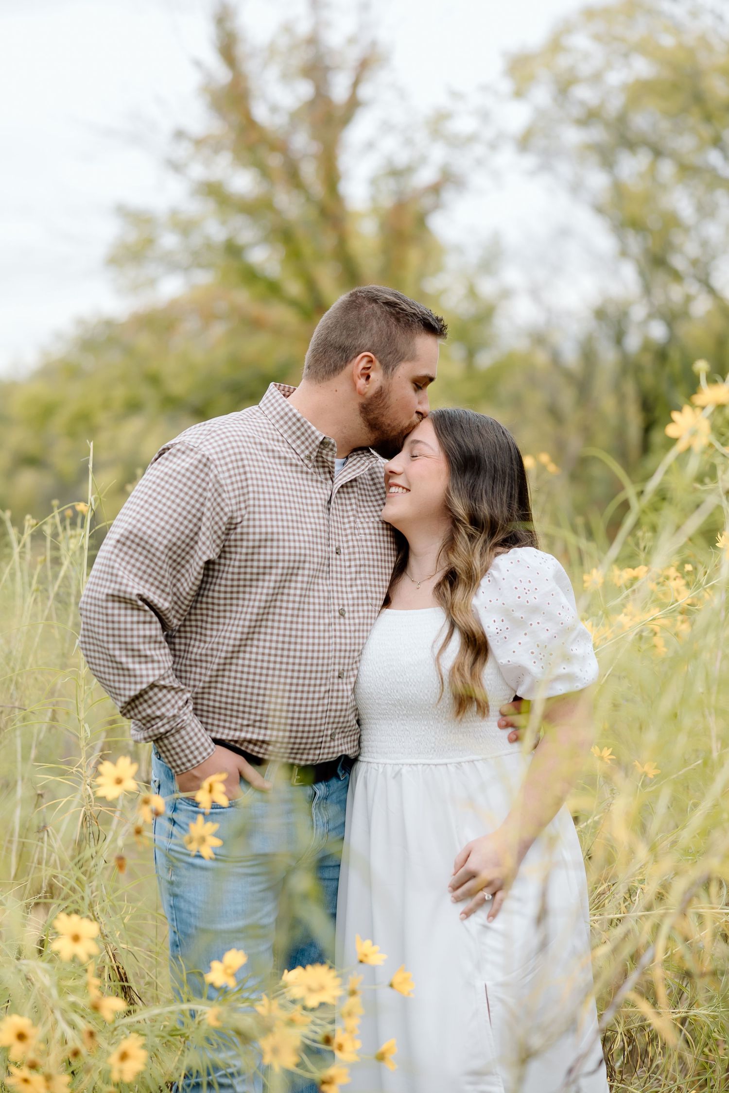 A couple shares an intimate moment among yellow wildflowers in a natural field setting.