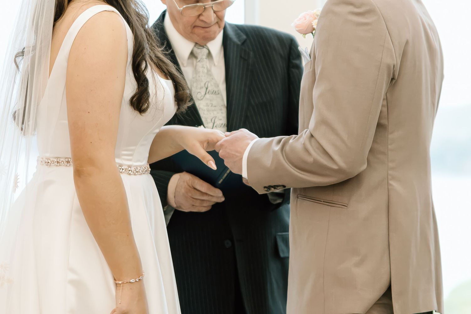 A wedding ceremony shows hands exchanging rings with an officiant presiding over the intimate moment.