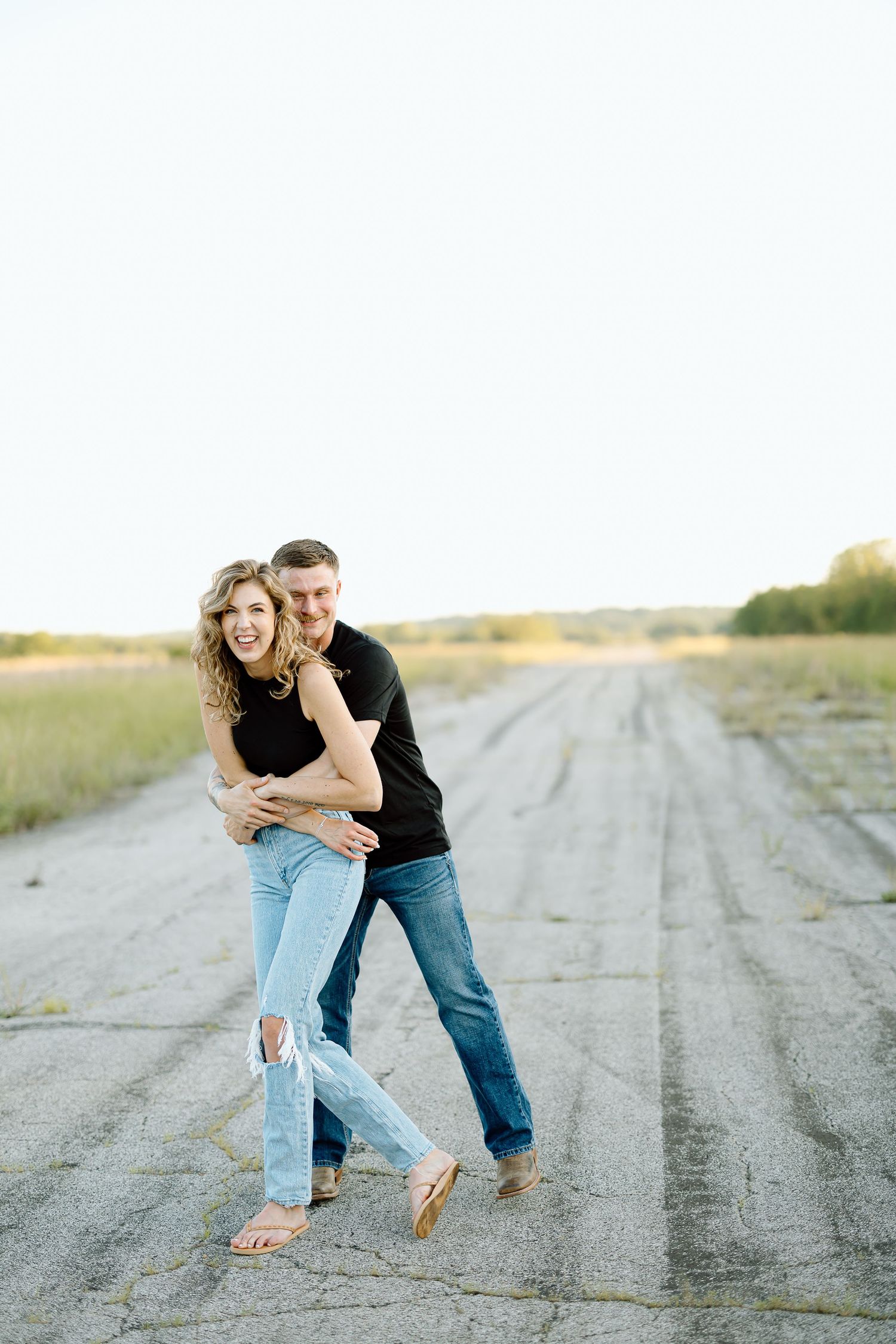 A couple shares playful moments together on a dirt road in a series of candid engagement photos.