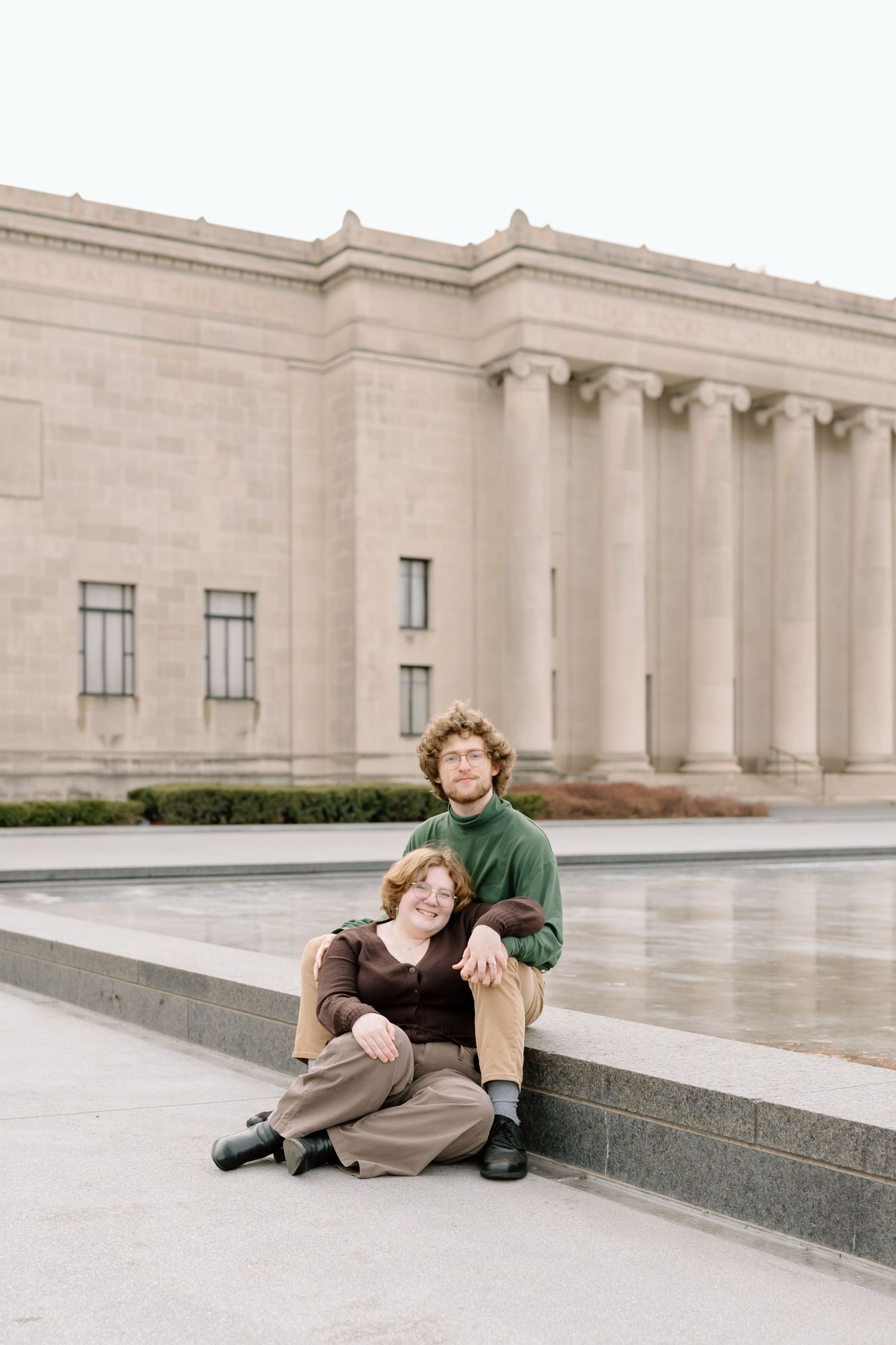Couple lounges together on marble steps of a stately building exterior.