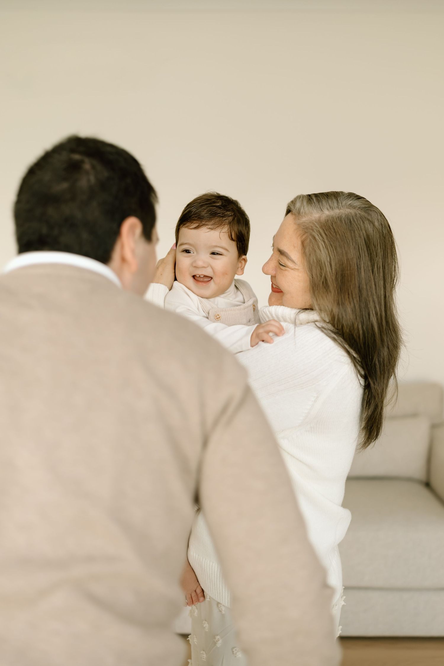A family shares joyful moments together on a white couch in a bright, minimalist setting.