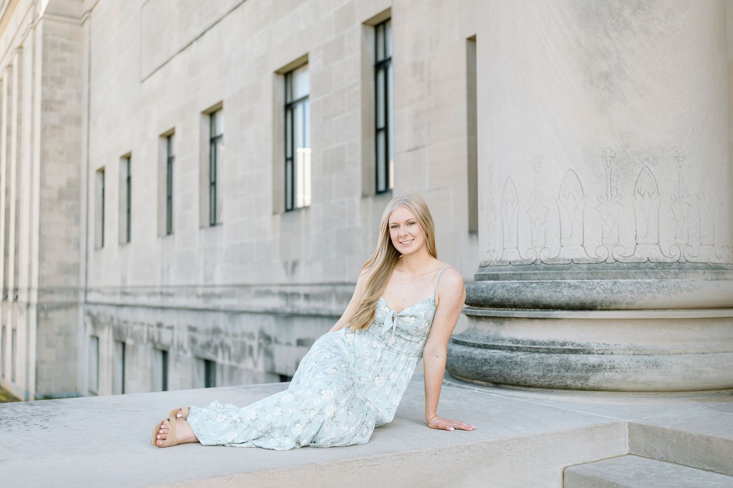 A woman in a light blue formal dress poses elegantly on stone steps during a photo session.