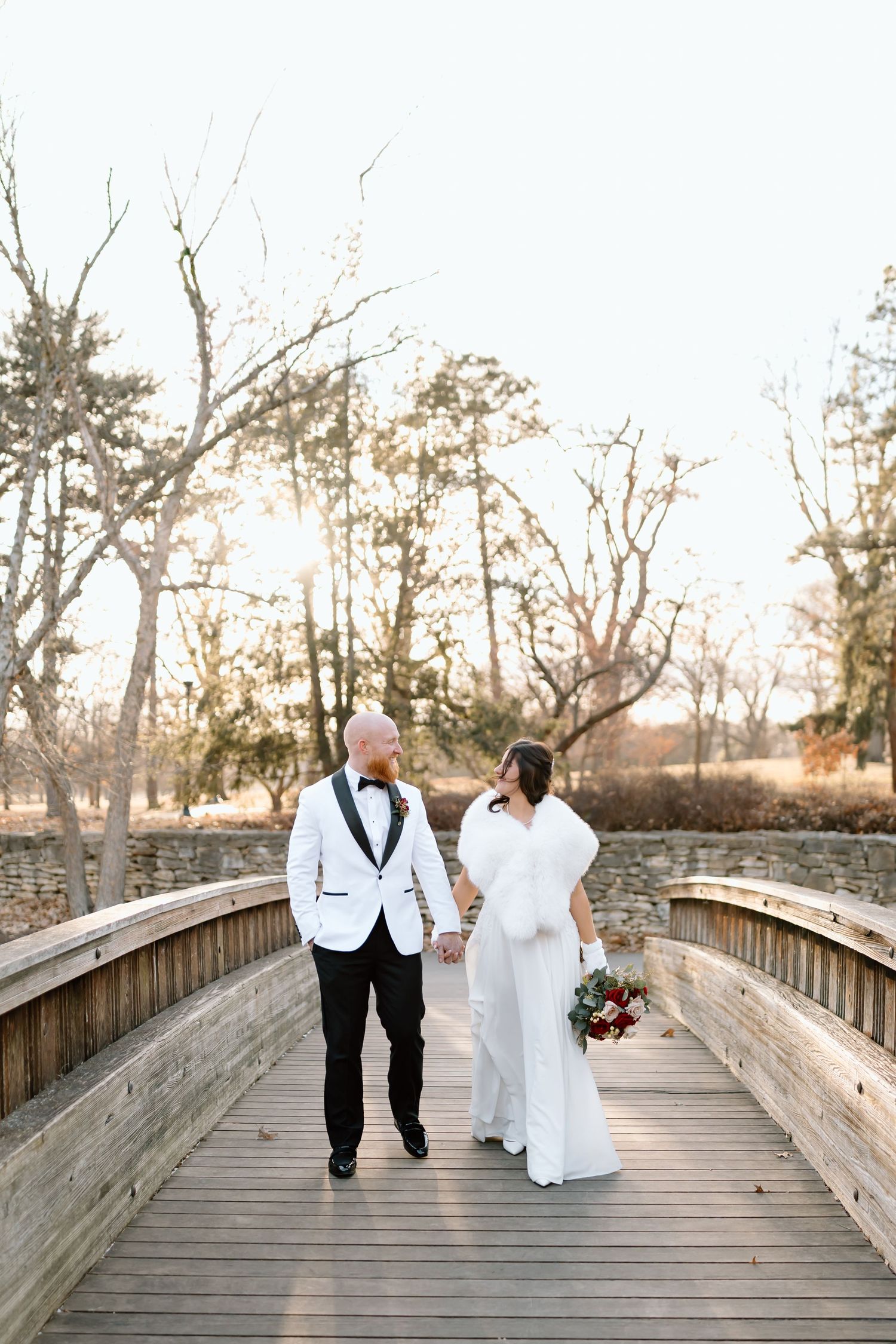 A couple walks hand in hand across a wooden bridge during sunset at their outdoor wedding ceremony.