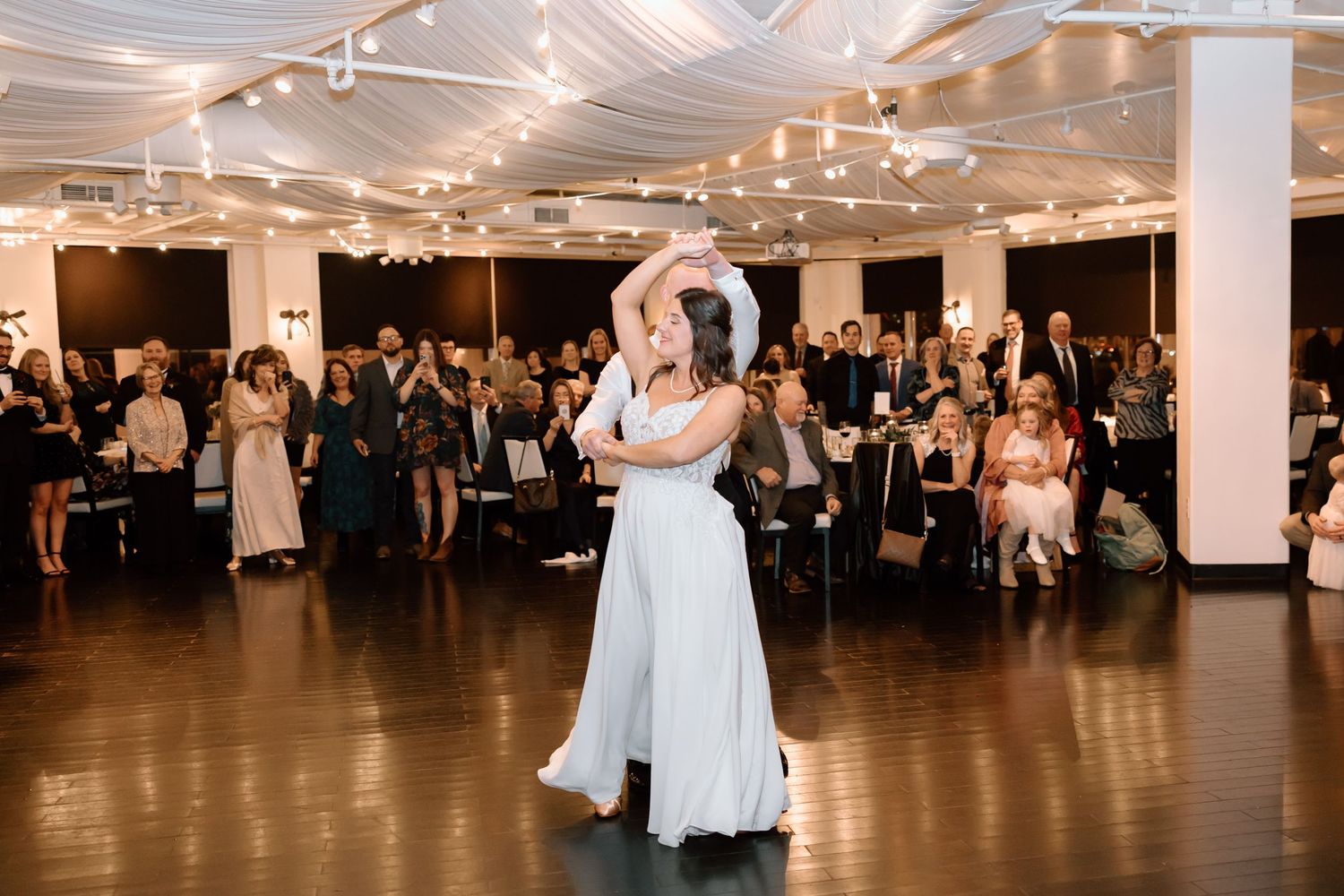 Wedding guests dance and celebrate on an elegant ballroom dance floor under warm lighting at an evening reception.