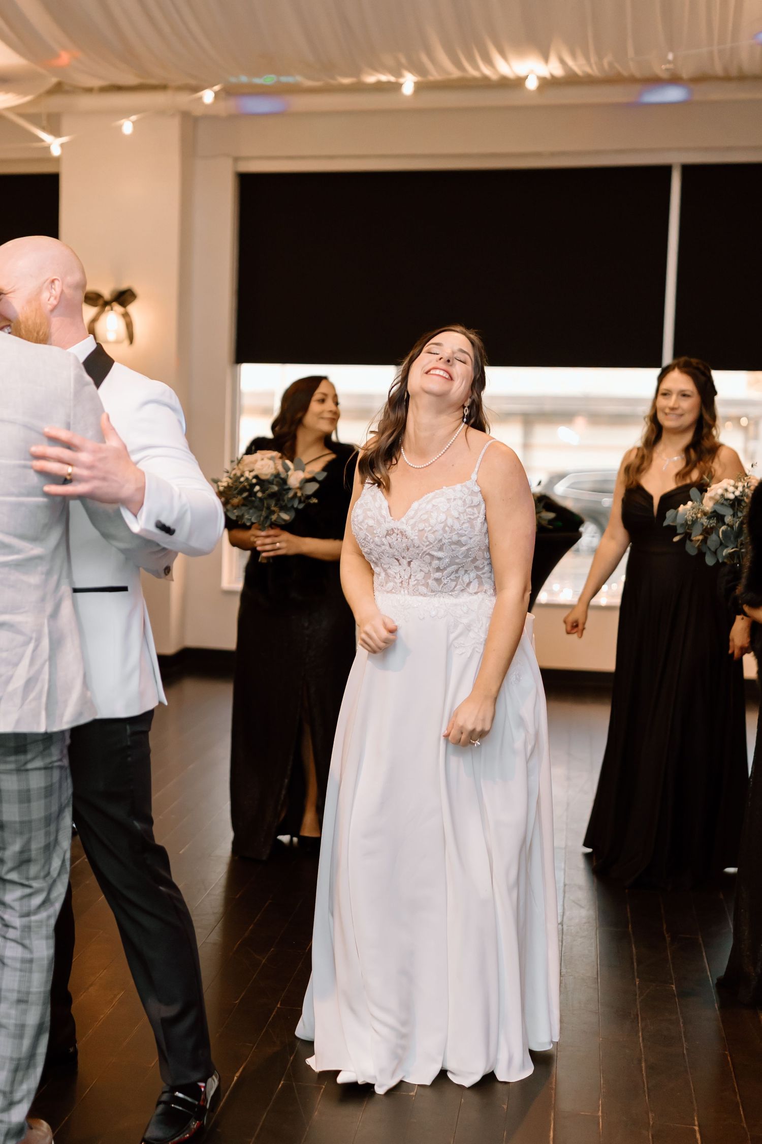 Wedding guests dance and socialize on a dark wooden floor at an elegant indoor reception venue.