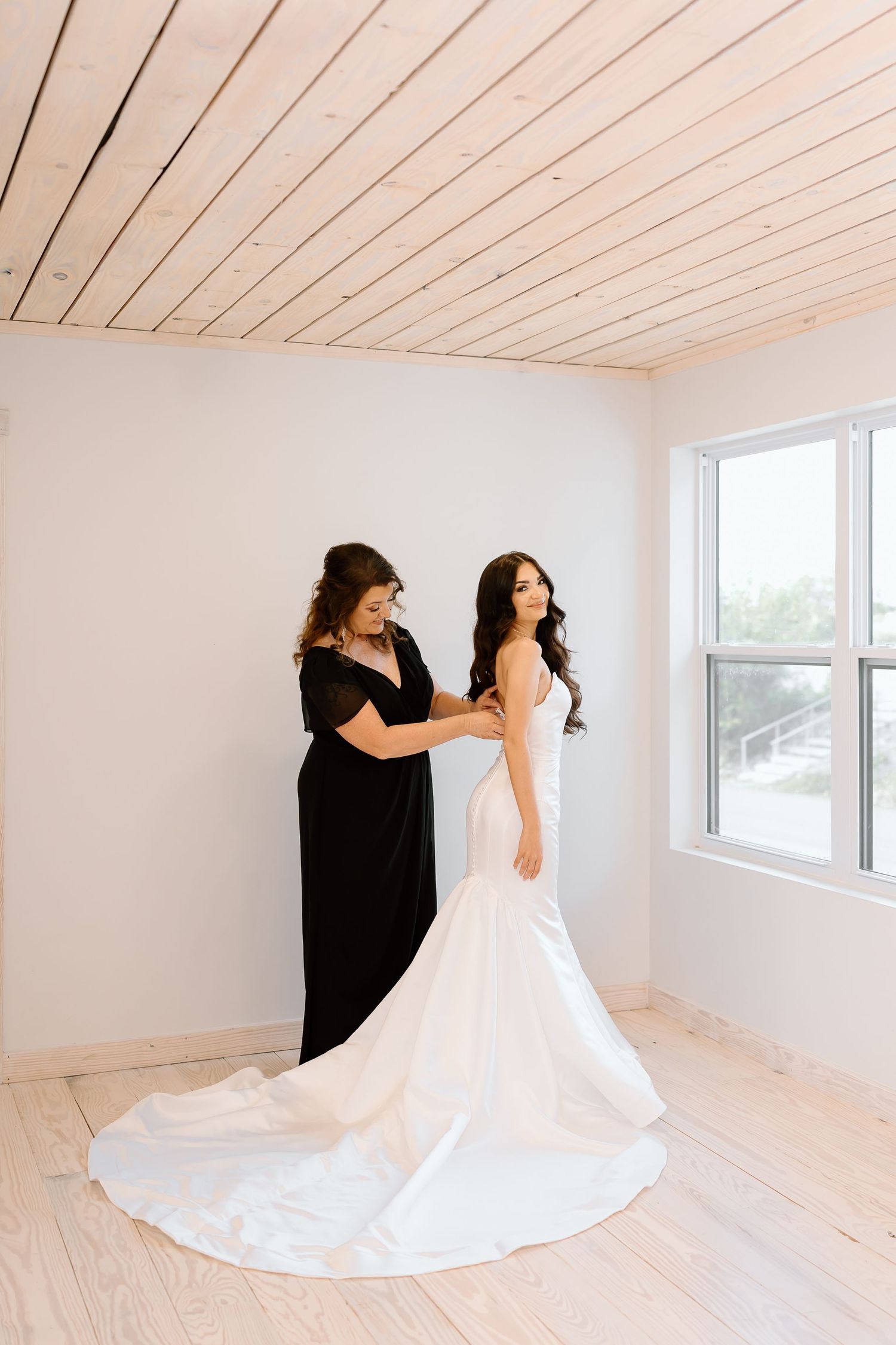 A bride in a flowing white wedding dress twirls gracefully in an empty room with light wood floors and white walls.