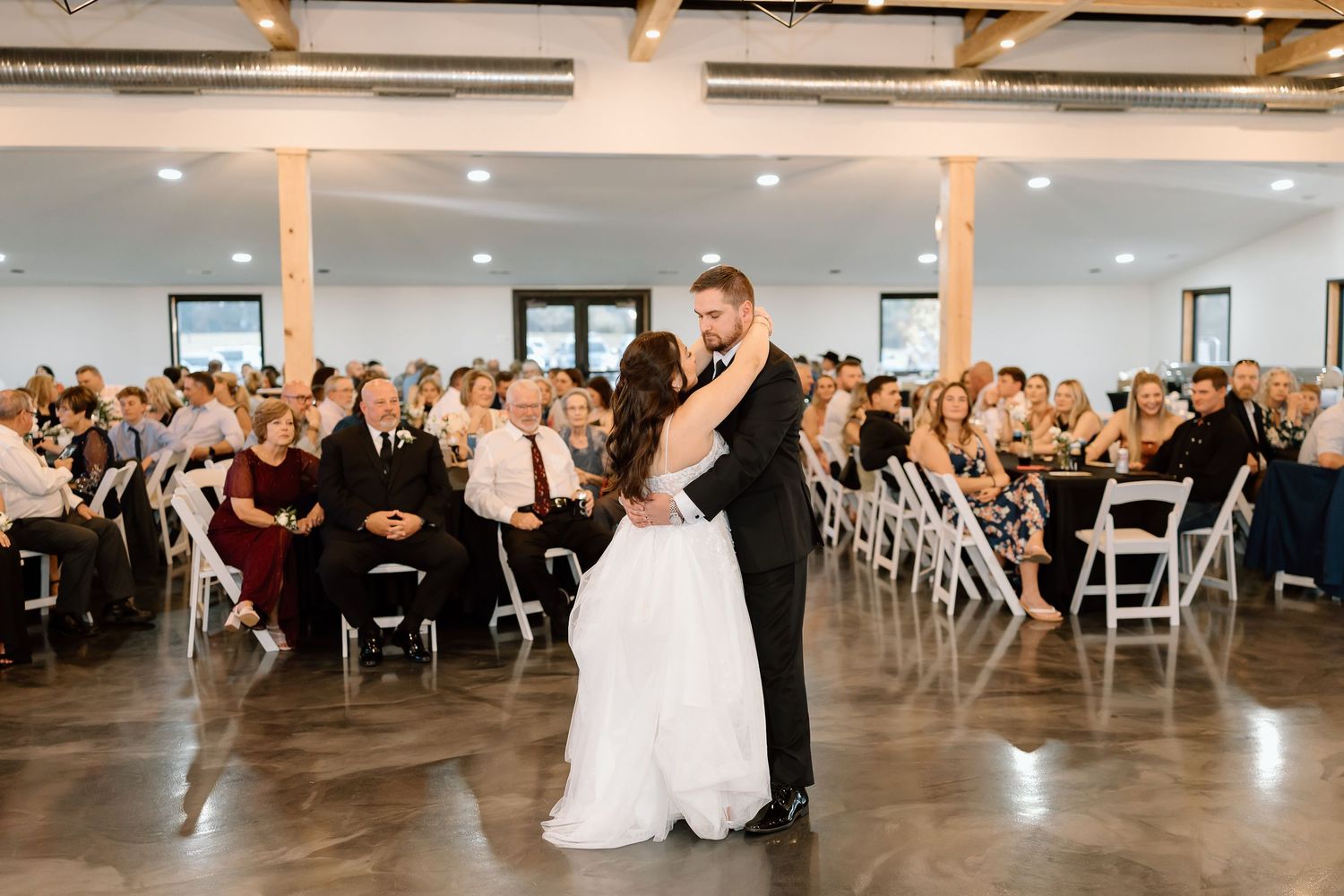 A sequence of wedding reception dance moments captured in a modern venue with white folding chairs and wooden pillars.