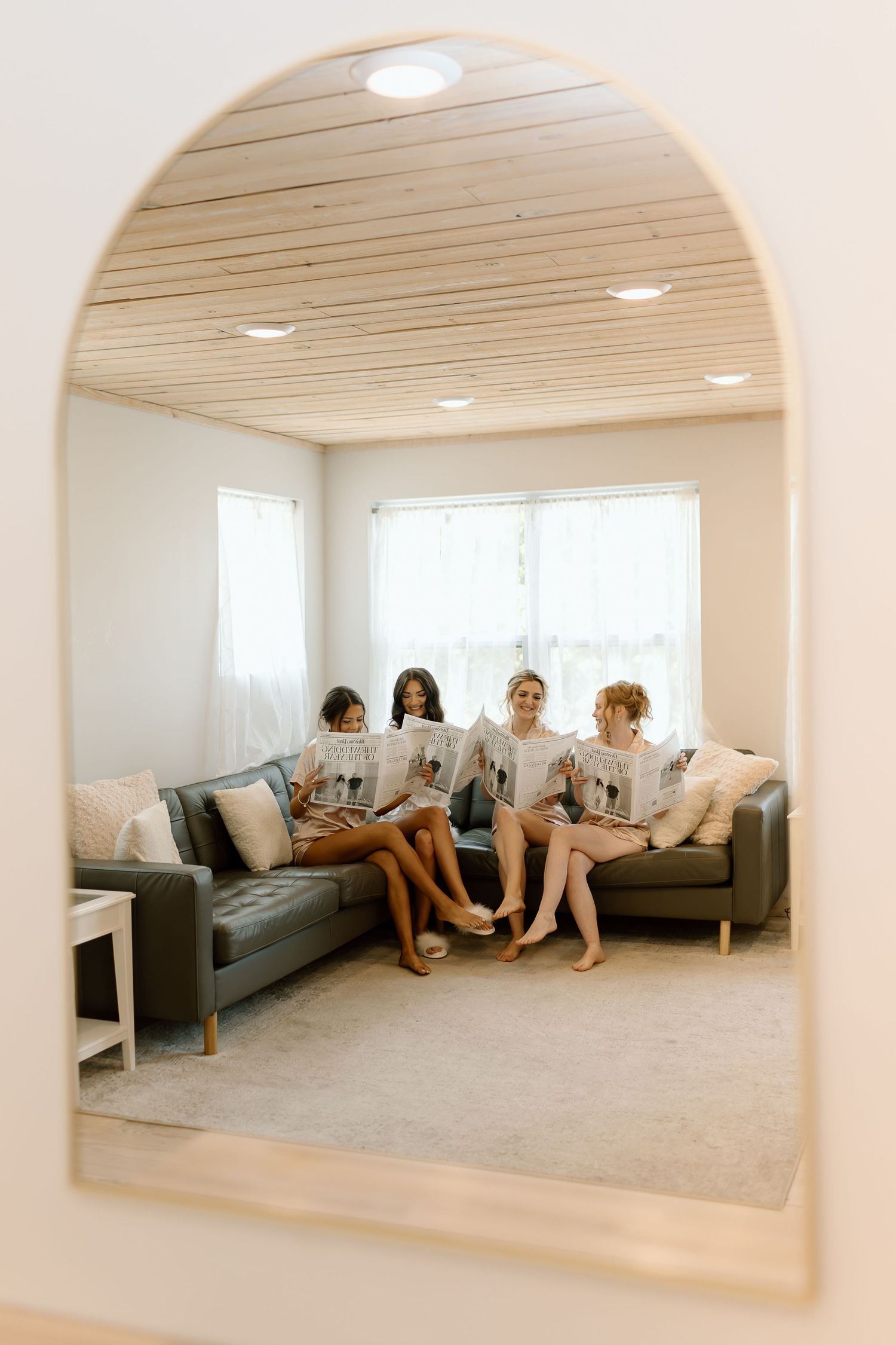 Four people relax on gray couches in a modern white room with arched doorways and recessed lighting.
