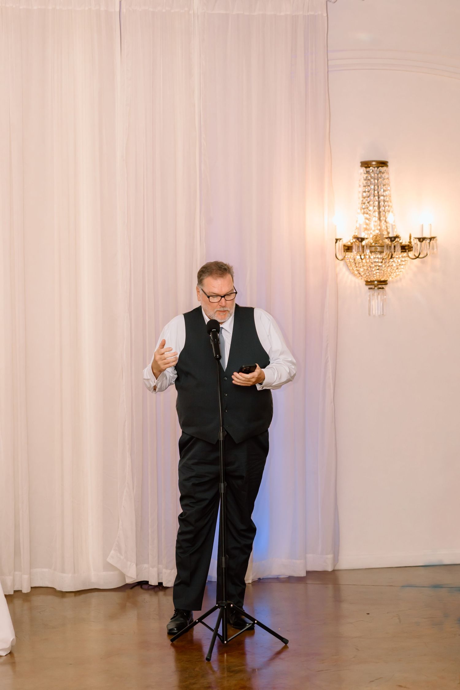 A performer in a black vest and white shirt stands in an elegant room with crystal chandeliers in a sequence of poses.