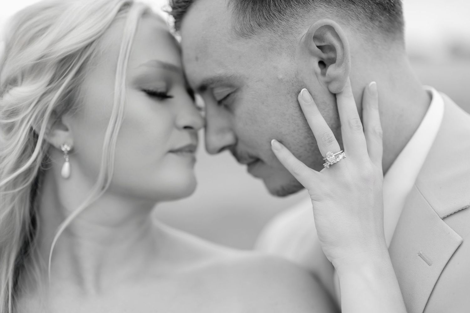Black and white wedding photo of bride and groom touching foreheads, showcasing diamond engagement ring.