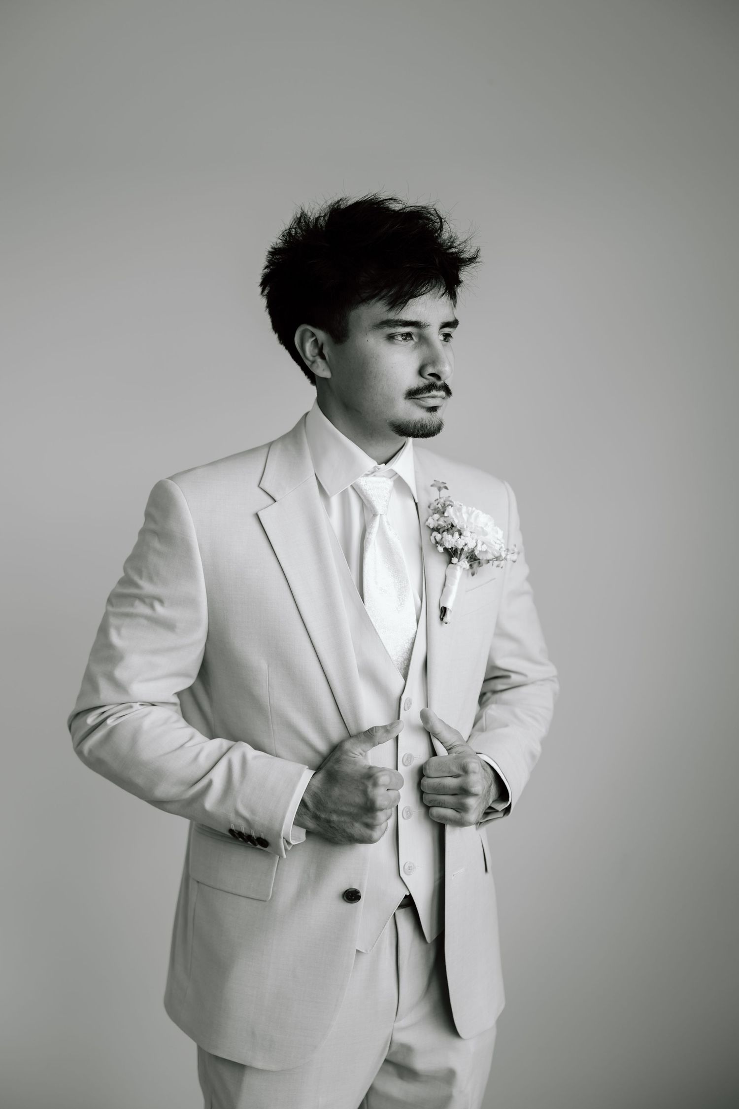 Elegant groom in a white suit with boutonniere poses confidently in a classic black and white wedding portrait.