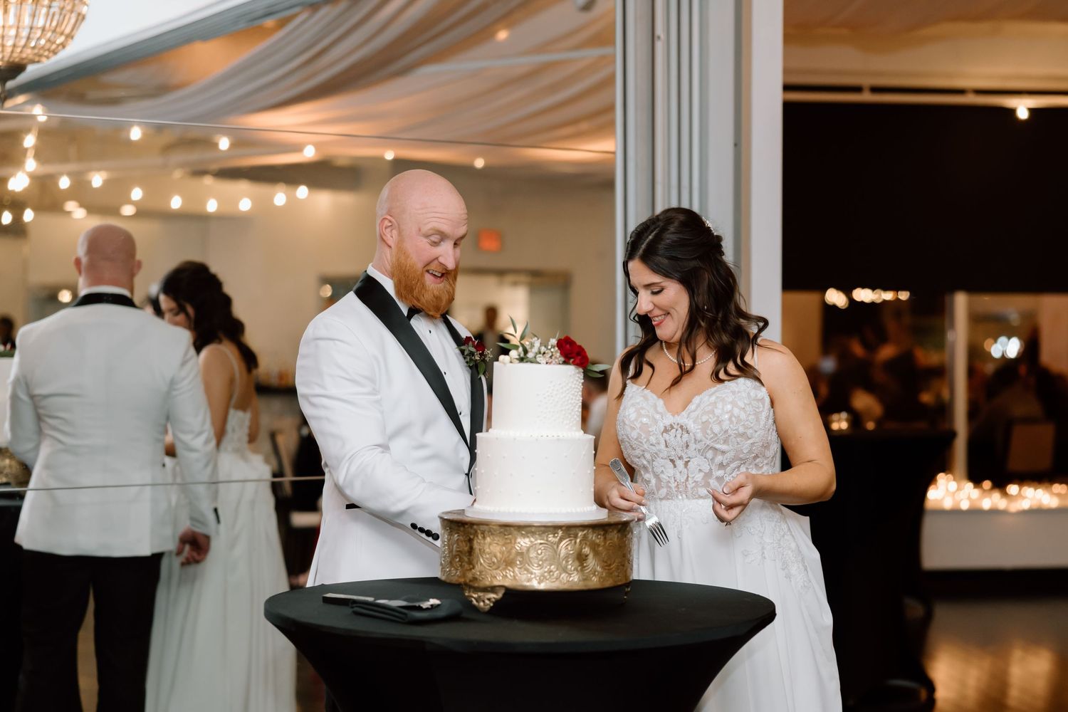 Bride and groom share a tender moment while cutting their elegant white wedding cake at their reception.