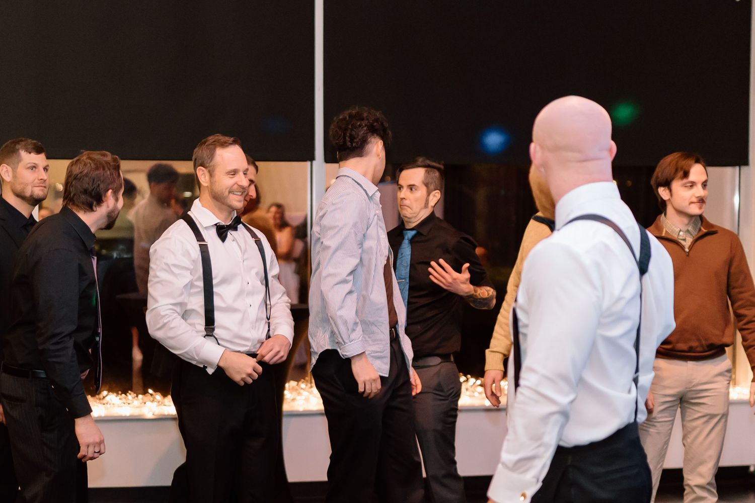 Guests in formal attire with suspenders and bow ties mingle at an elegant evening event.
