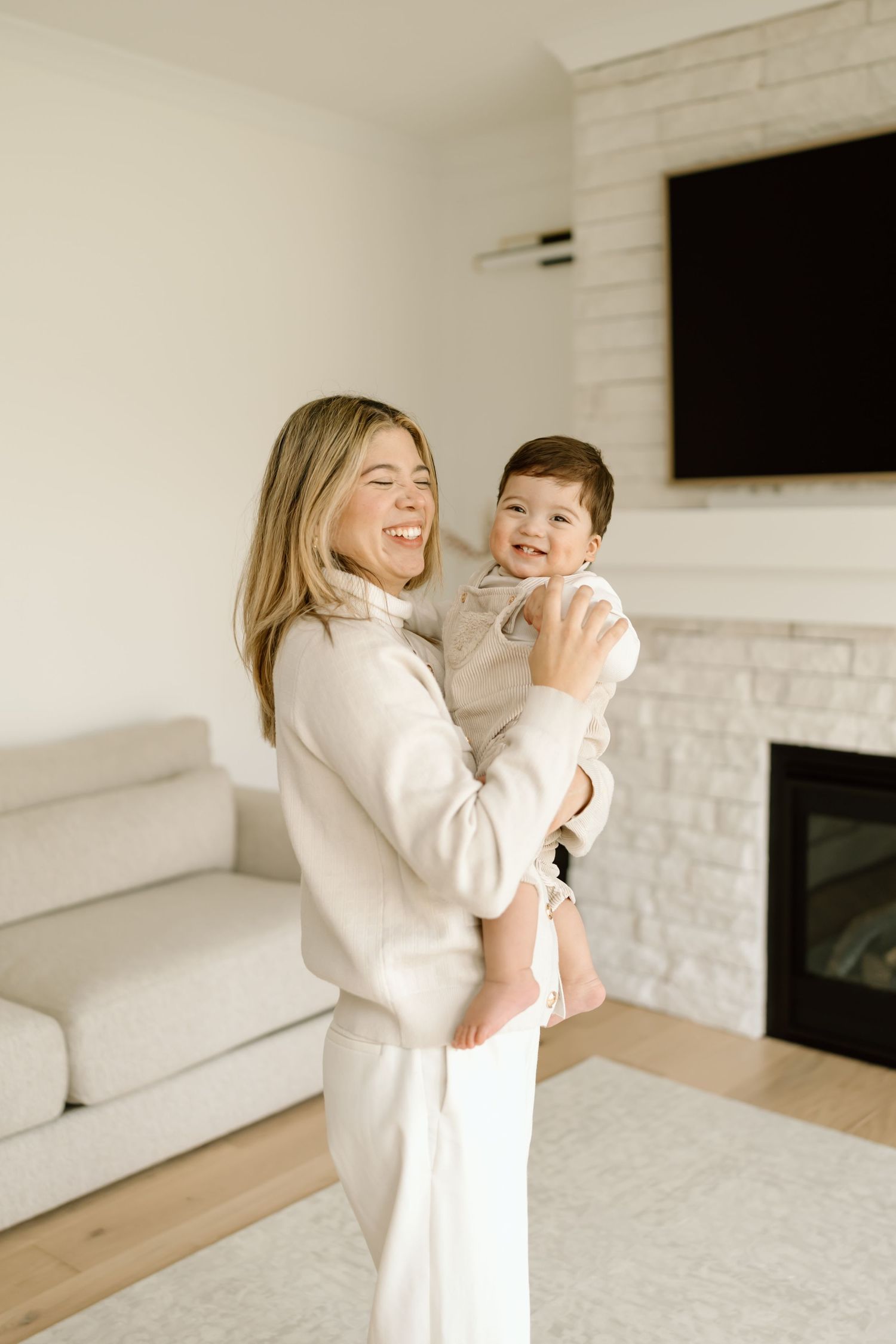 A joyful moment shared between parent and child in a bright living room with white brick fireplace and hardwood floors.