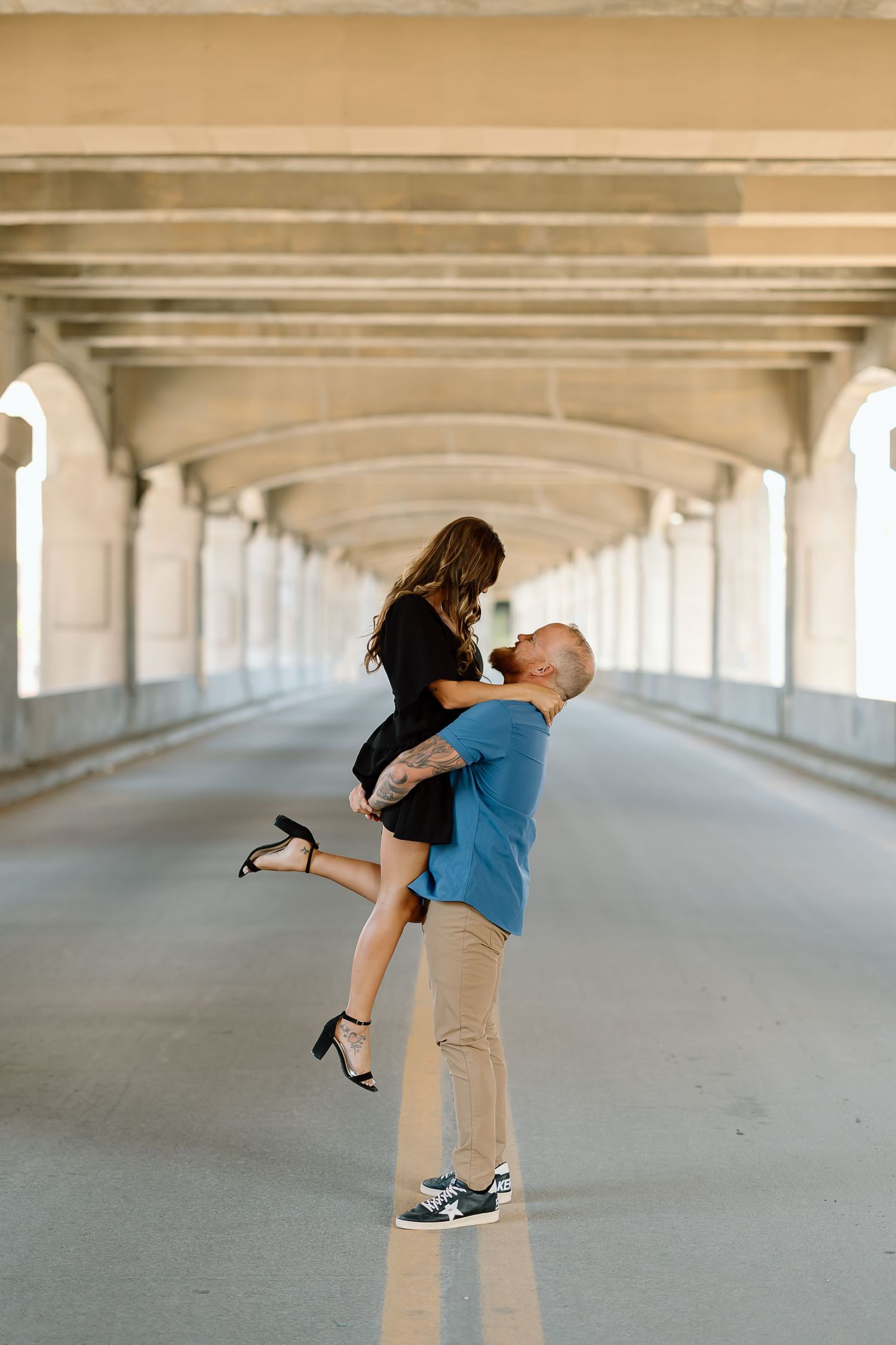 A couple embraces romantically under a concrete bridge structure in a series of progressive engagement photos.