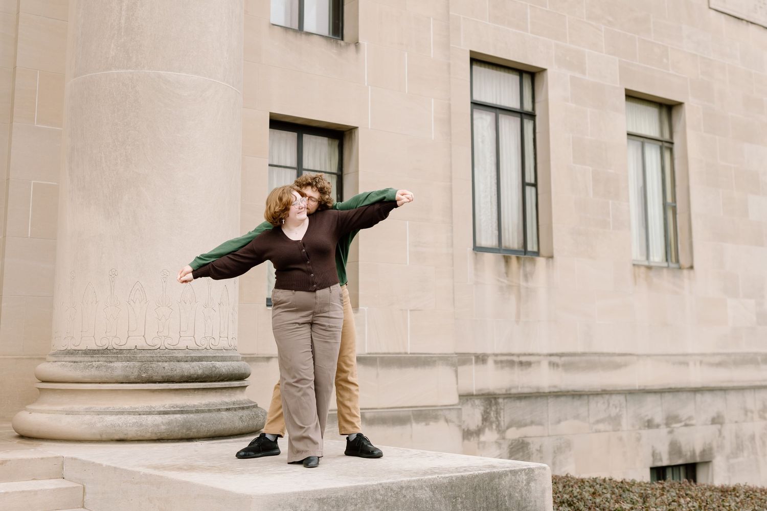 A person performs a parkour jump between concrete pillars outside a building with beige walls.