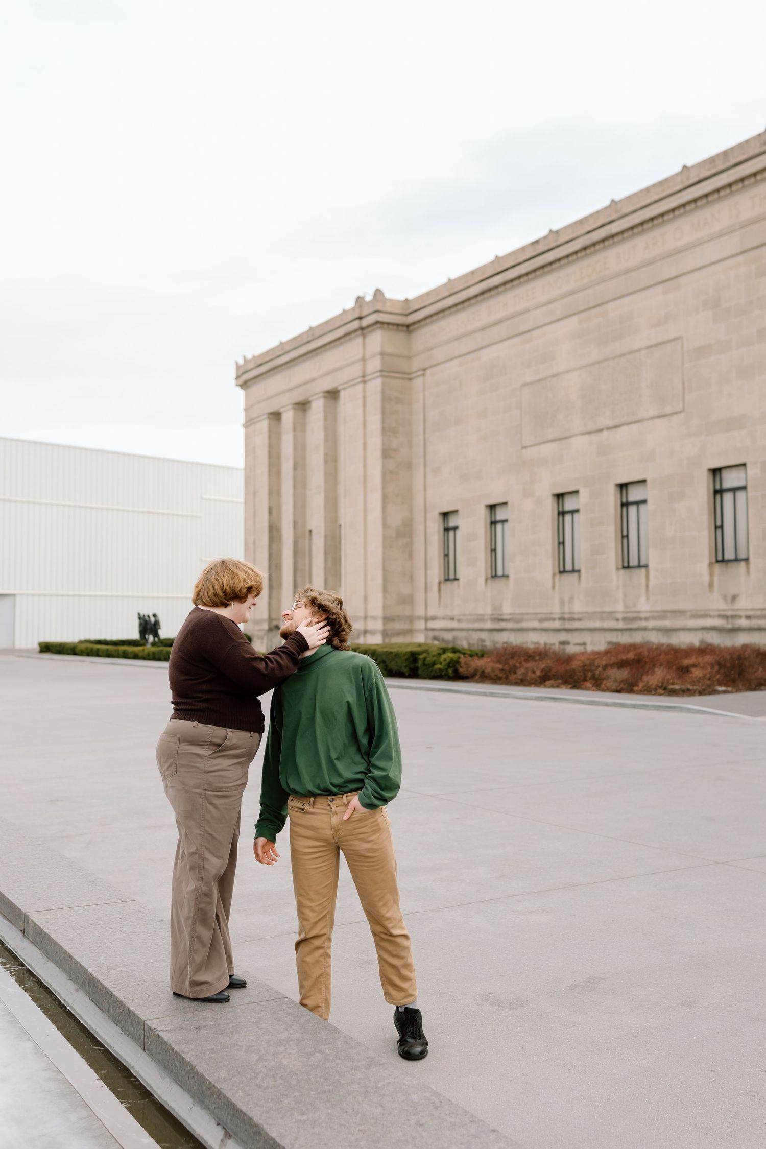 Two people walk along a concrete path next to a minimalist industrial building with tan stone walls.