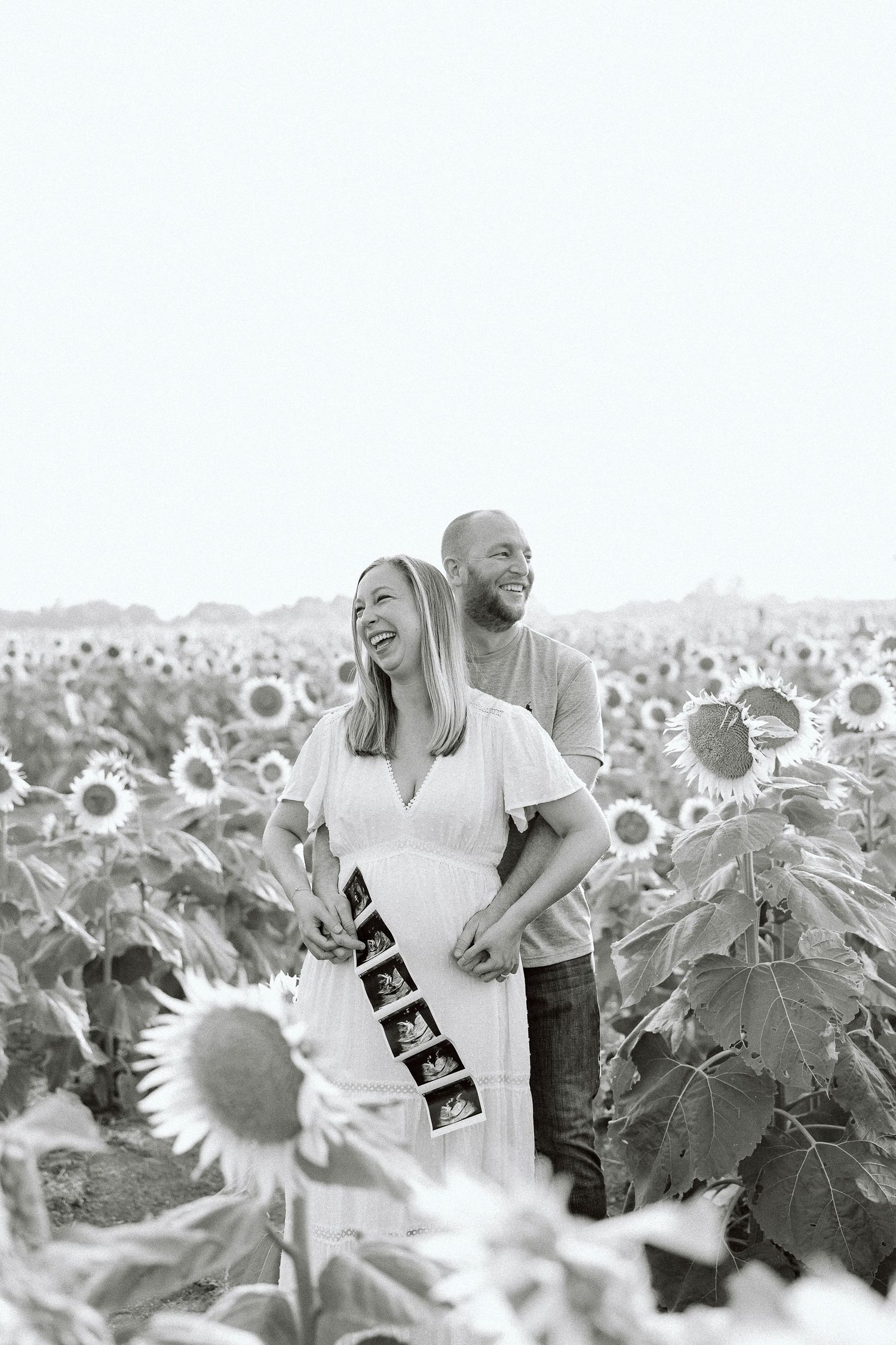 A joyful couple shares a tender moment together in a sunflower field, captured in black and white photography.
