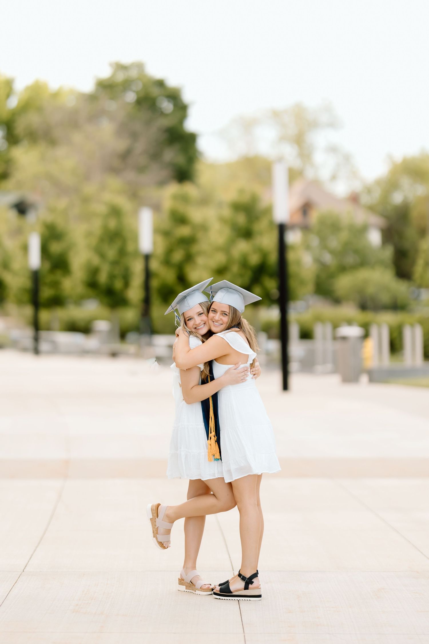 Two figures in white dresses share an embrace in a bright outdoor setting with lamp posts in the background.