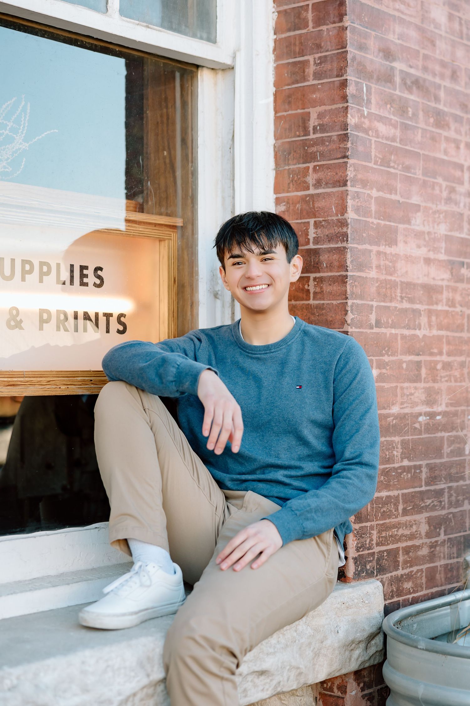 Relaxed portrait sitting on stone ledge by vintage storefront window.