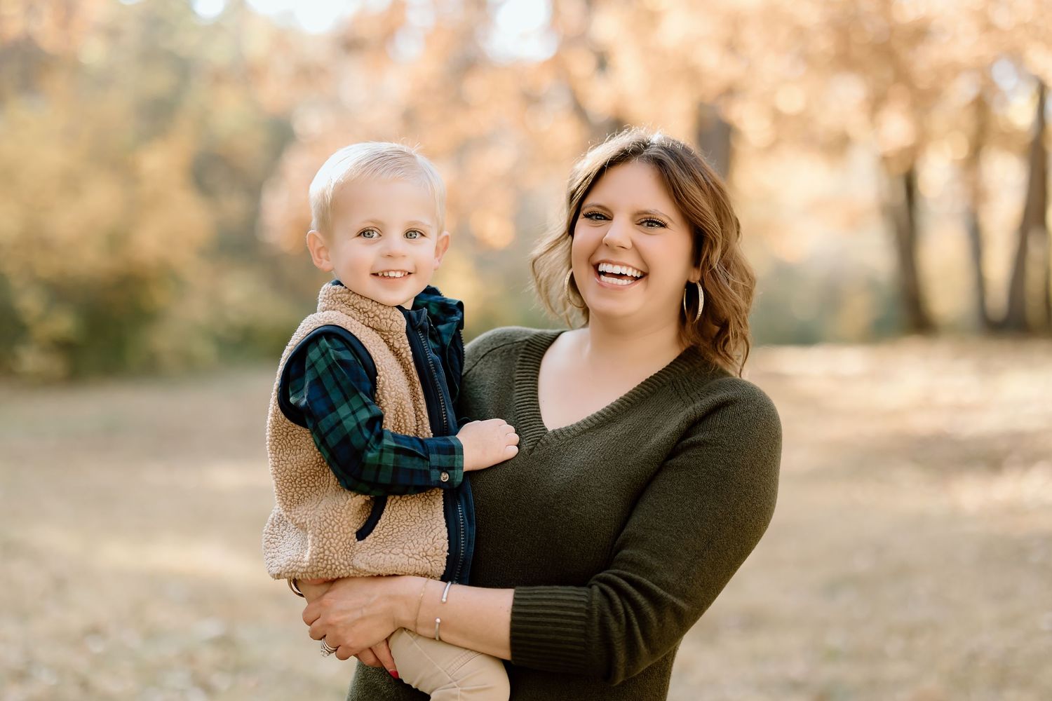 A joyful outdoor family photo shows a parent and child laughing together in warm autumn light.