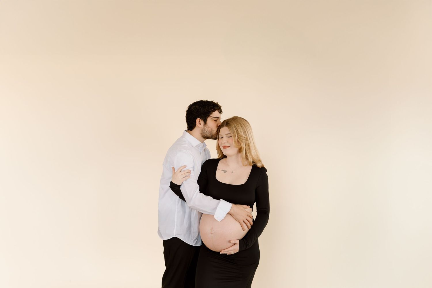 Intimate studio maternity portrait with couple sharing a gentle moment against neutral backdrop.