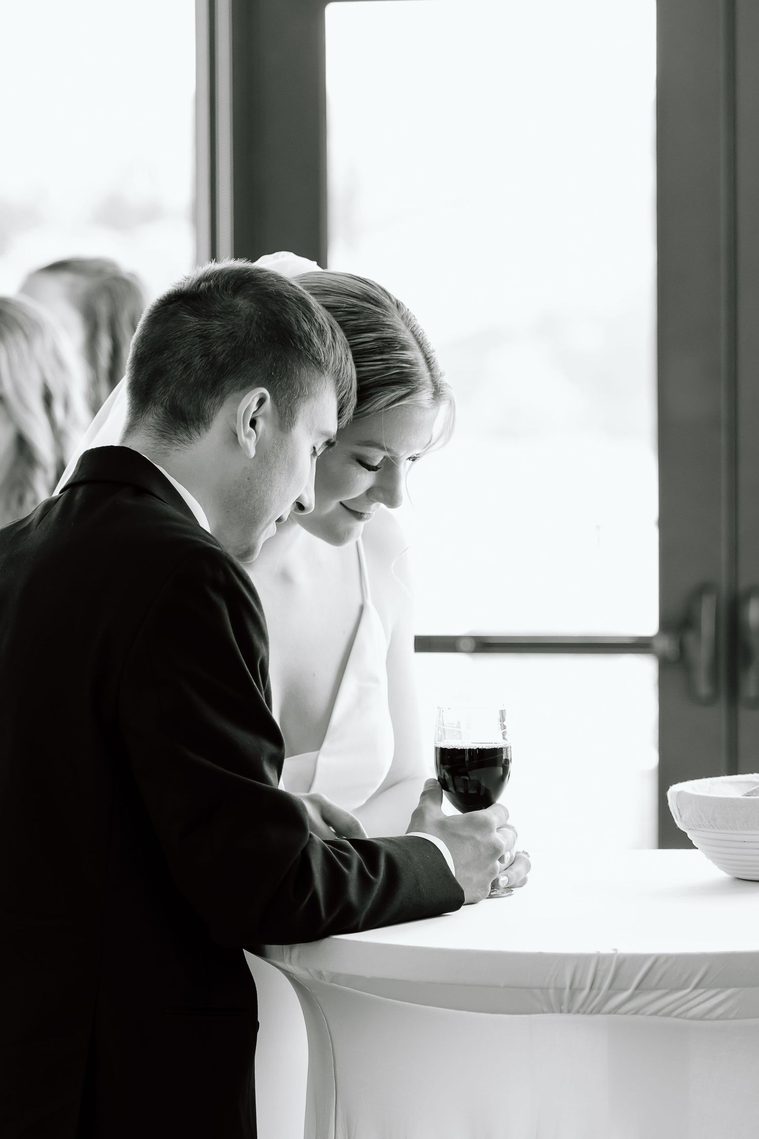 Two people in business attire lean over a white table in profile, engaged in focused discussion at a meeting.