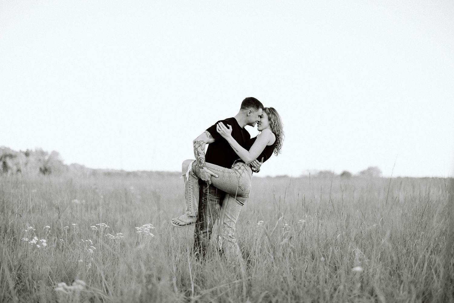 A black and white photo series showing a romantic couple embracing in a grassy meadow at sunset.