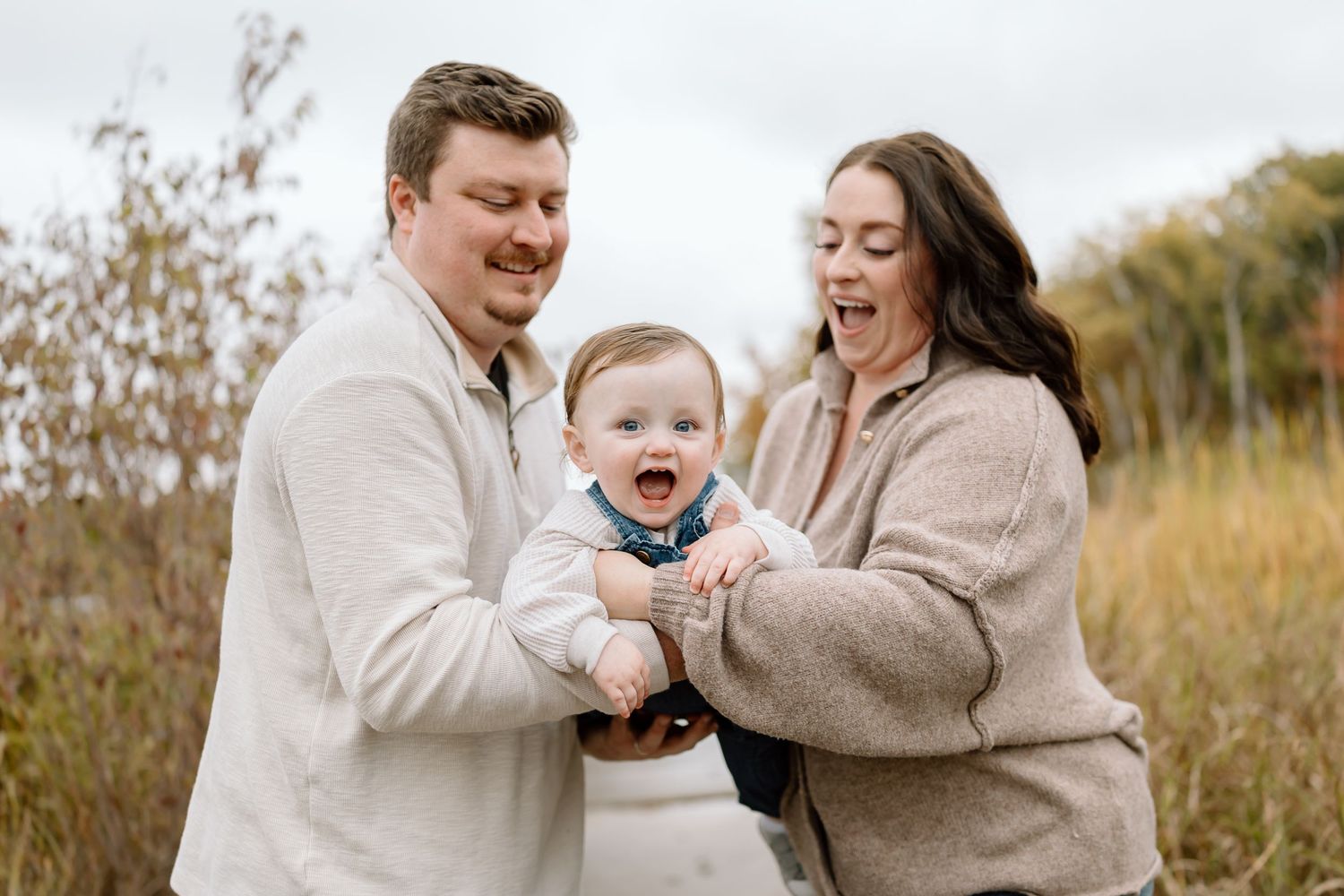 A family shares joyful moments together in a golden autumn field wearing neutral colored sweaters.