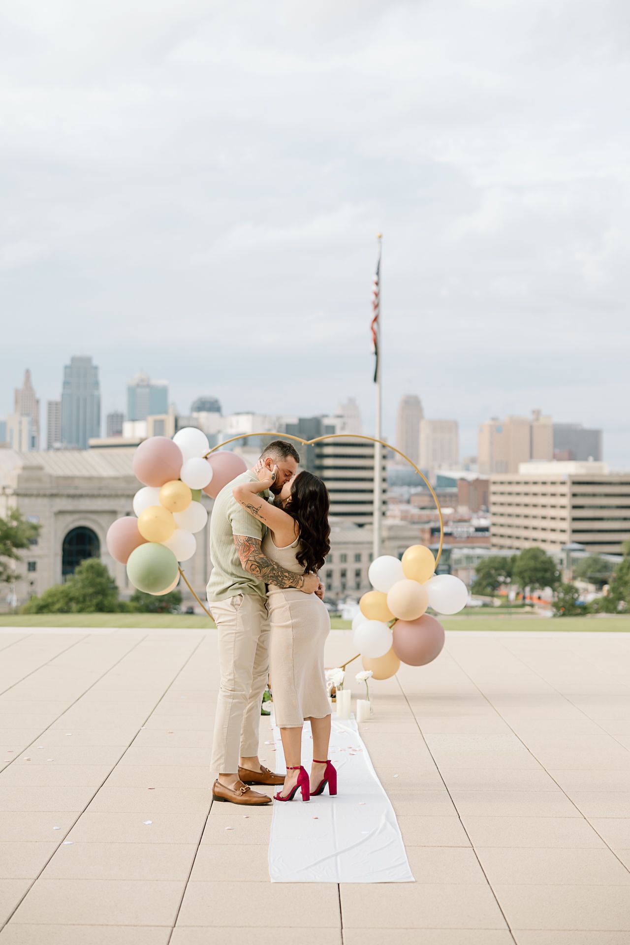 Romantic rooftop photoshoot with pastel balloons and city skyline backdrop.