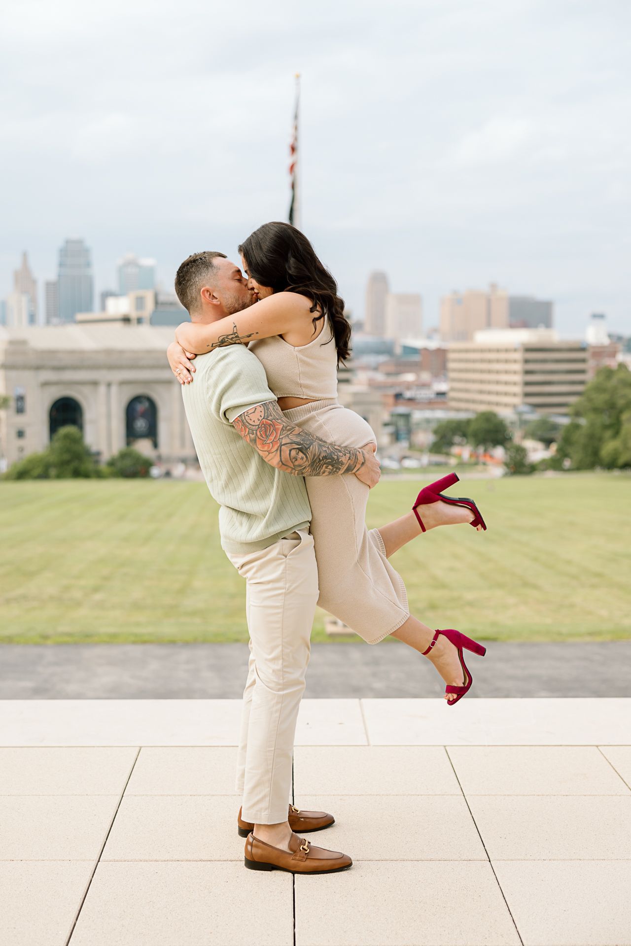 A couple shares playful poses and embraces on an outdoor terrace with an urban landscape in the background.