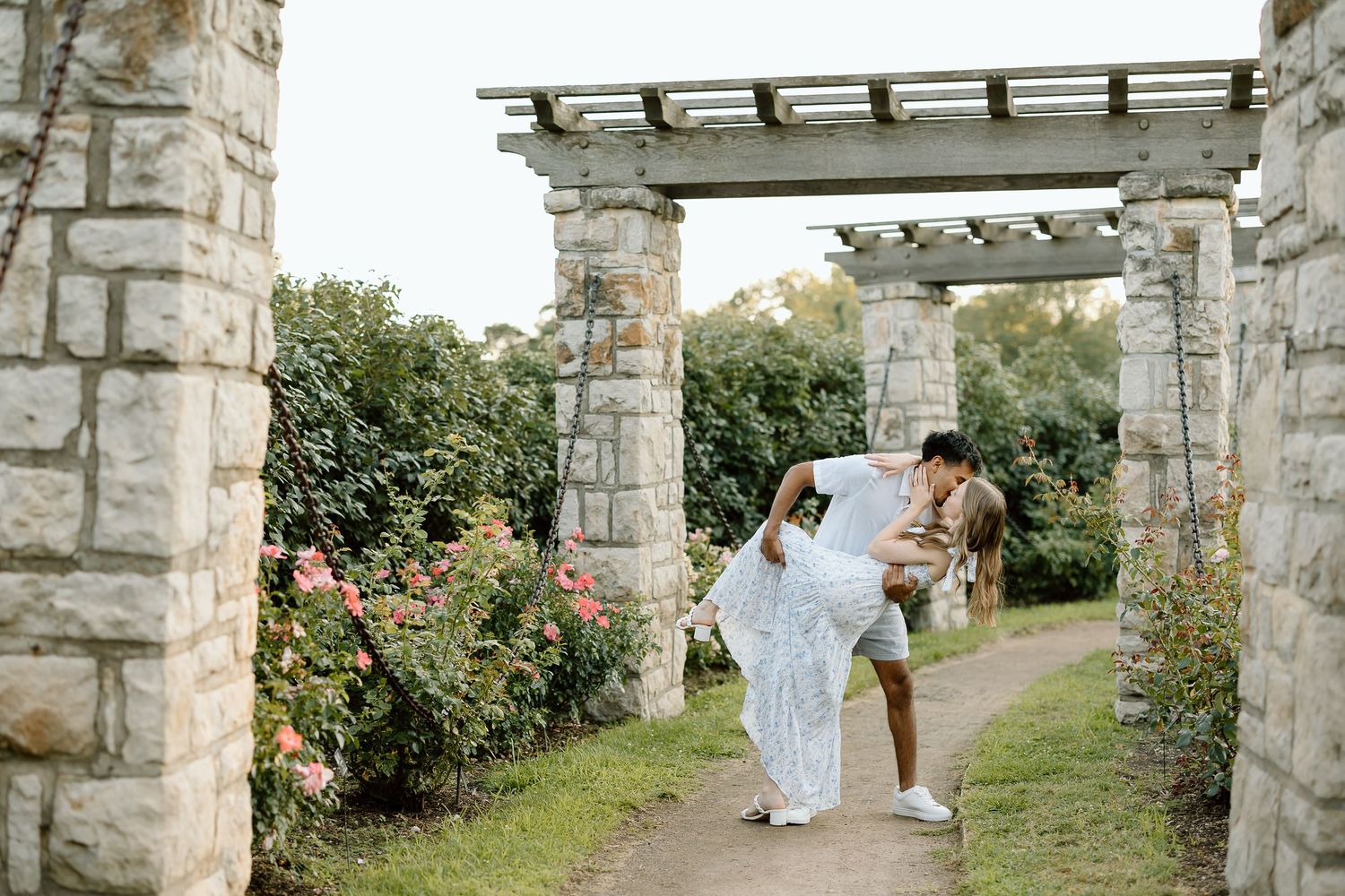 A stone archway in a garden creates a romantic pathway with figures walking in the distance.