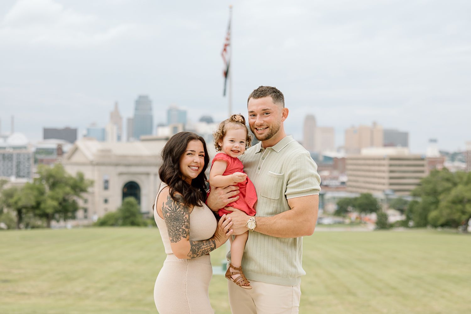 A family shares joyful moments together on a grassy hill overlooking a city skyline during a sunny afternoon.