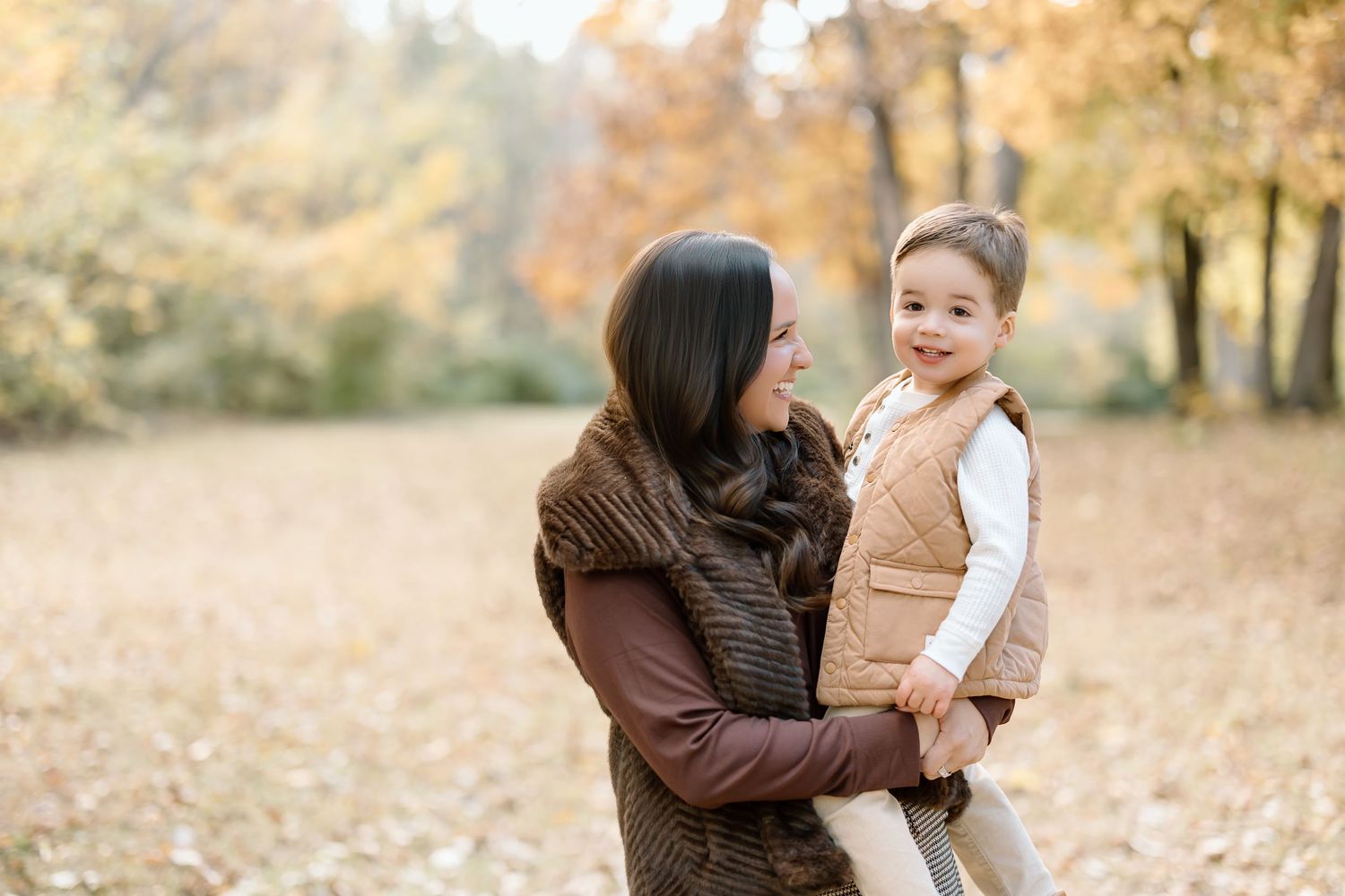 A parent and child share a tender moment together while playing in autumn leaves during golden hour.