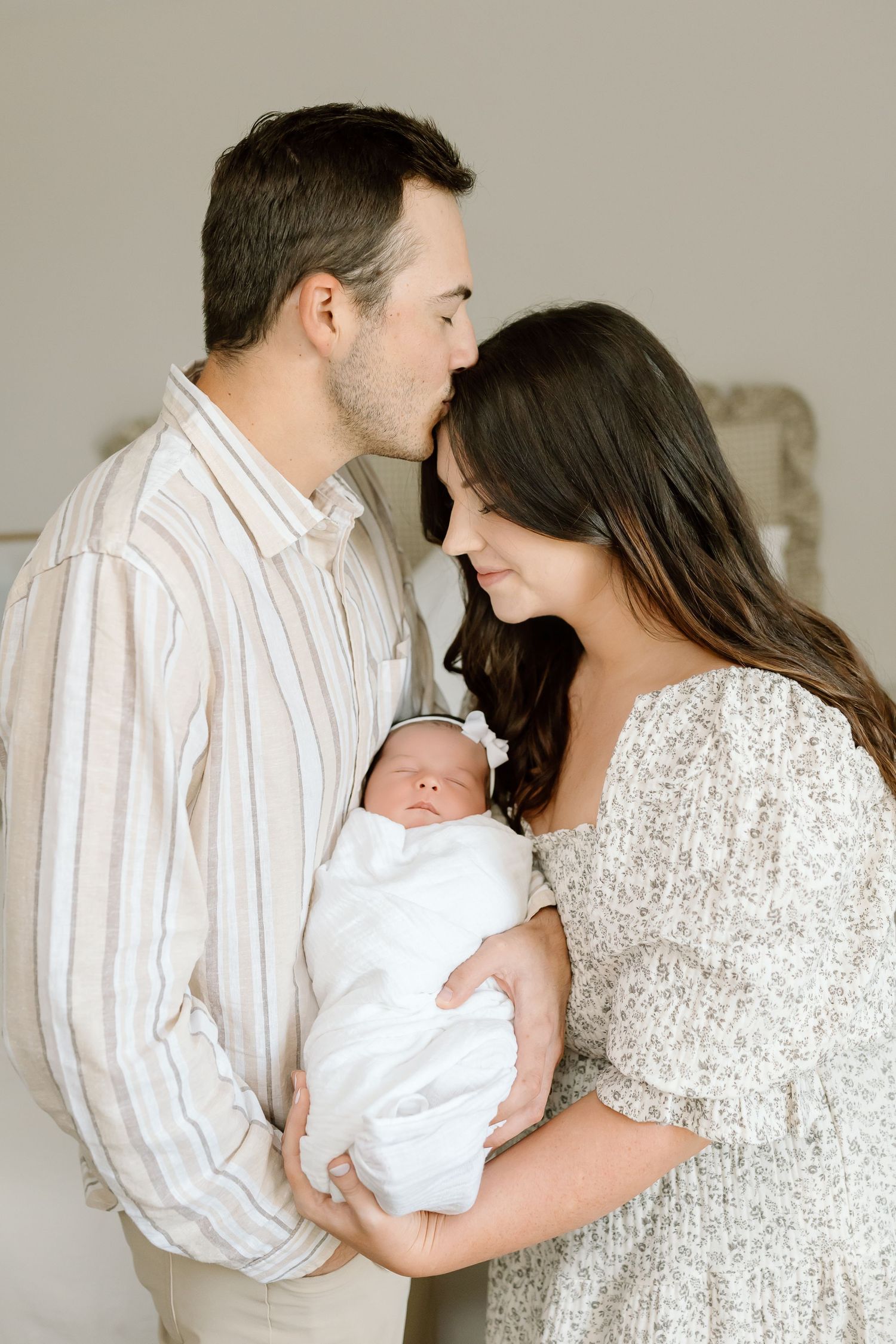 A series of intimate family portraits showing parents cradling their newborn baby in white clothing against a neutral backdrop.